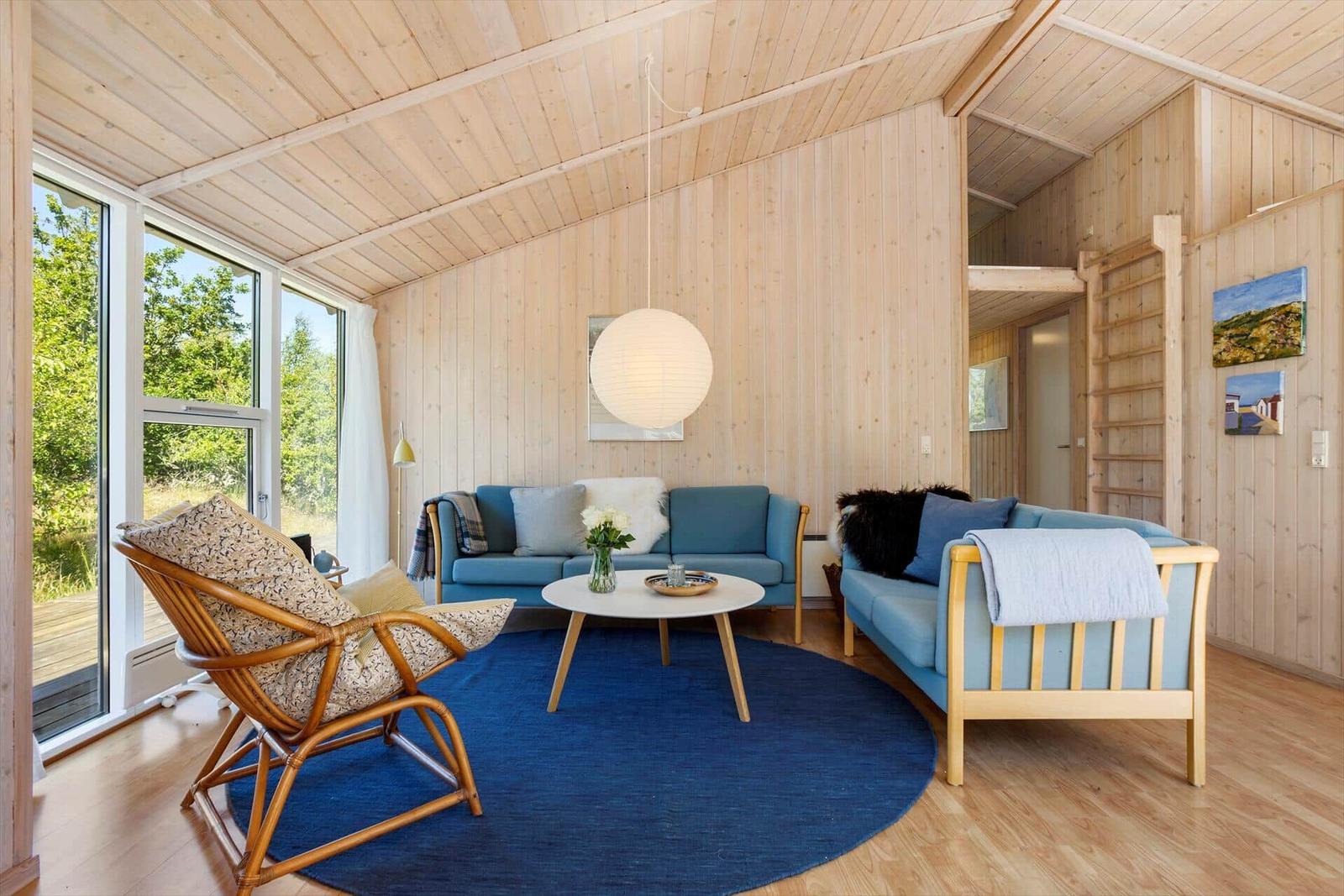 Living room with wooden walls, blue sofas, and round rug.