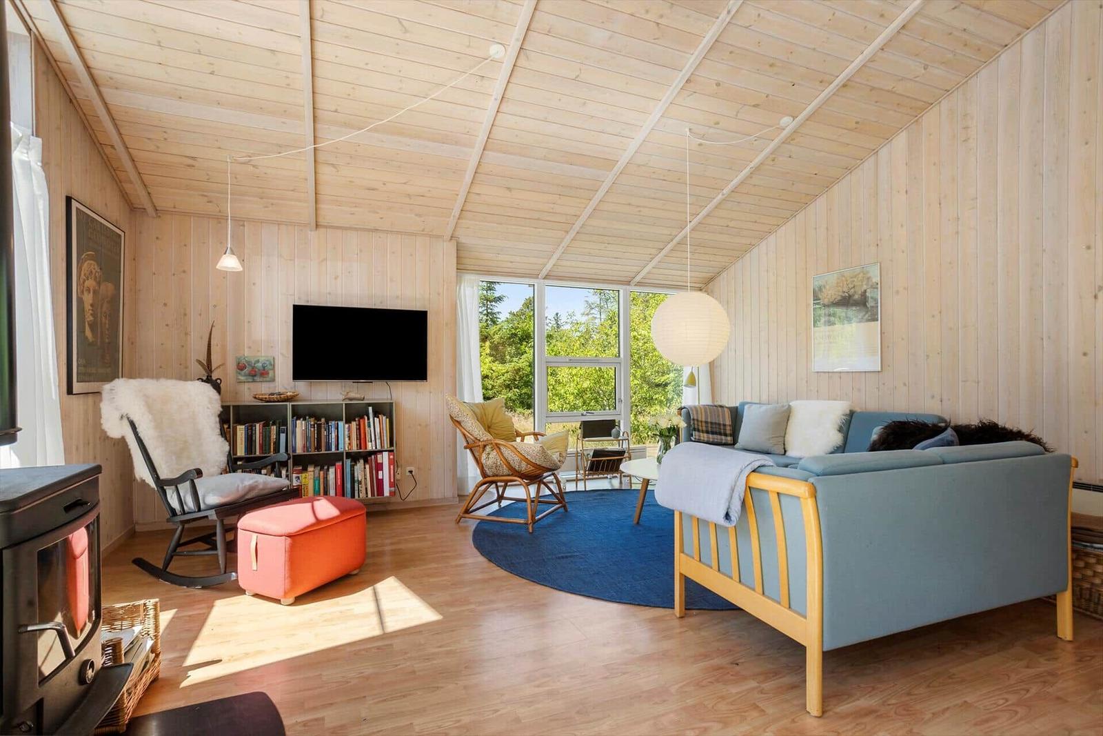 Living room with wooden walls, sofa, TV, and view of greenery.