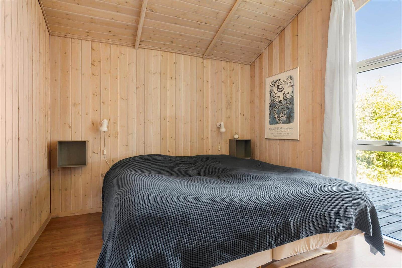 Bedroom with wooden walls, bed, and window view of greenery.