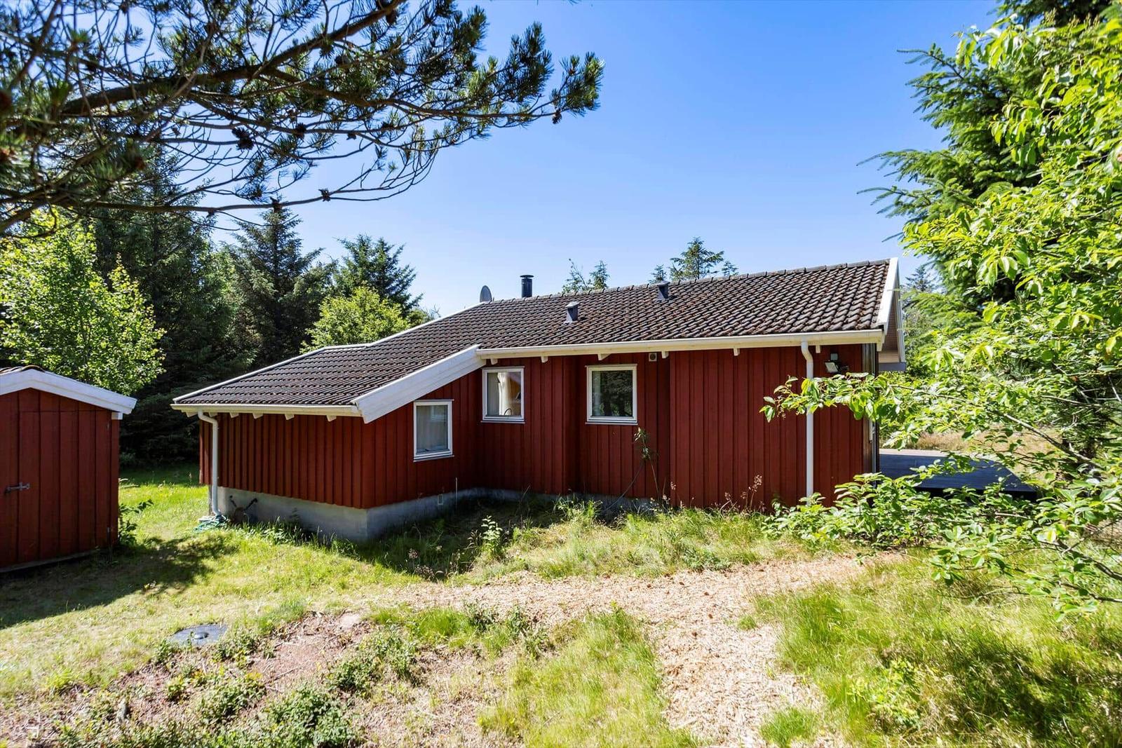 Red wooden house with brown roof, surrounded by grass and trees.