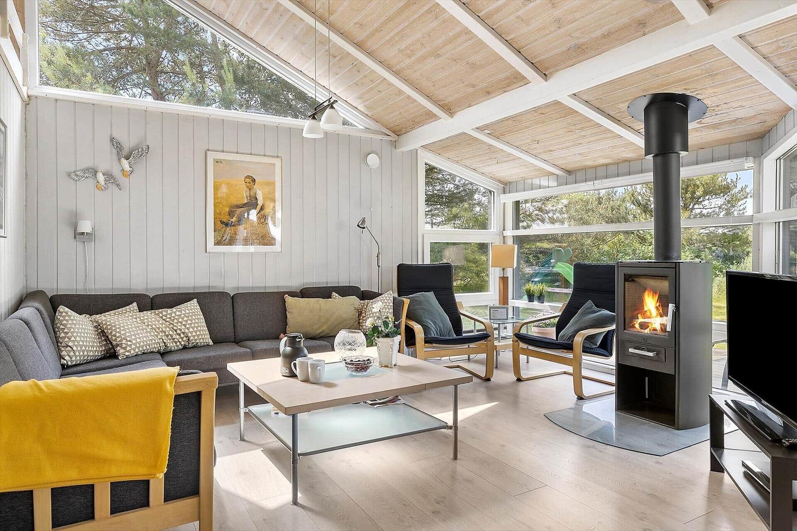 Wohnzimmer mit Sofa, Sesseln, Kamin und großen Fenstern.