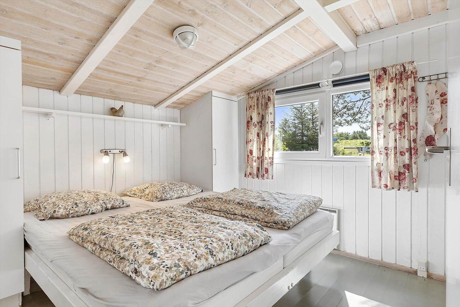 Schlafzimmer mit Doppelbett, Fenster und Holzdecke.