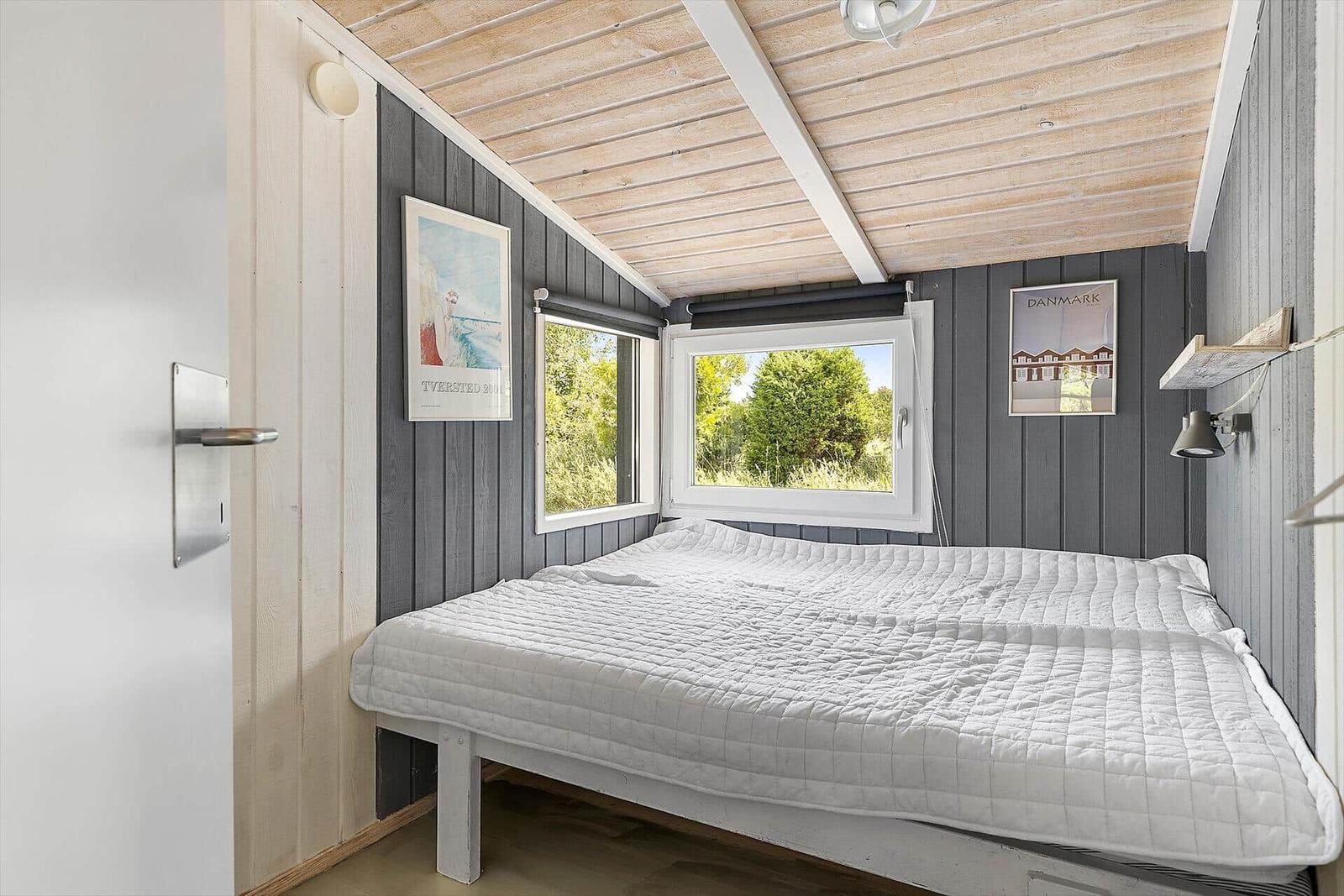 Schlafzimmer mit Bett, Fenstern und Holzdecke.