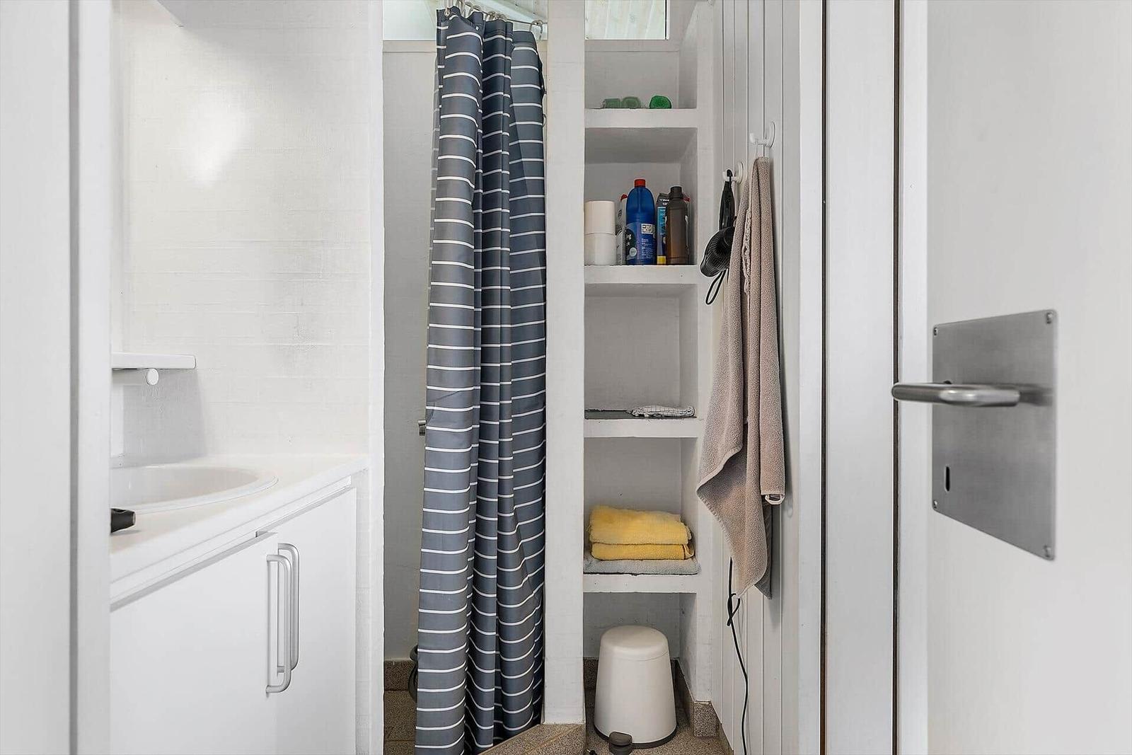 Badezimmer mit Dusche, Waschbecken und Regal für Badutensilien.