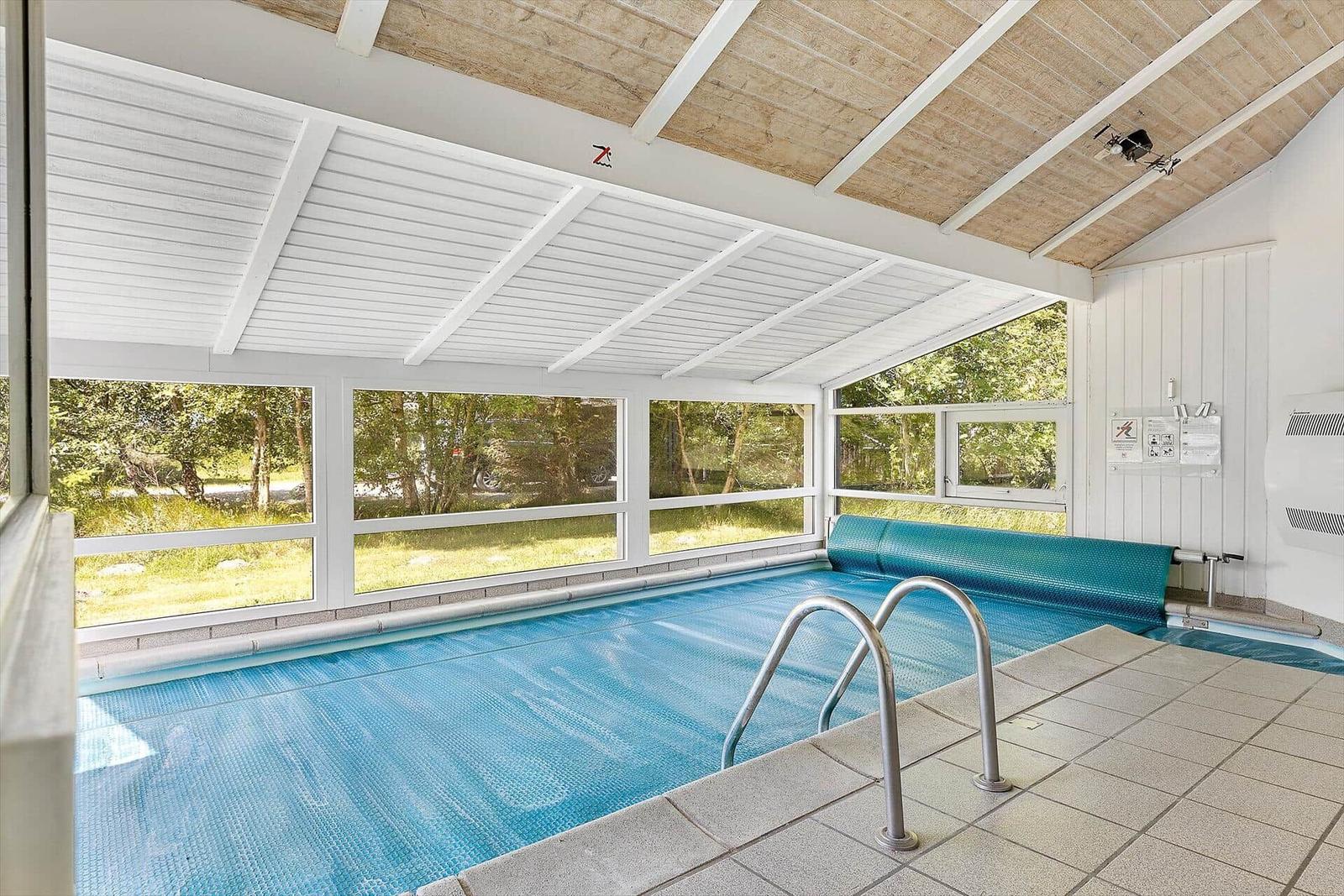 Innenpool mit Glaswänden und Holzdecke. Schwimmbecken mit Metalltreppe.