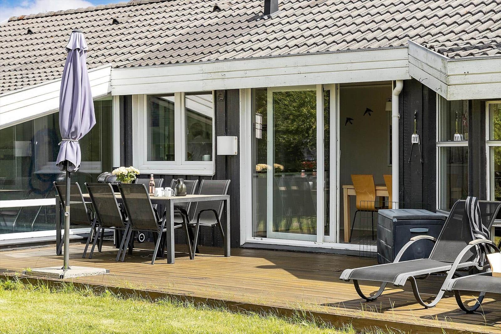 Terrasse mit Tisch, Stühlen und Liegestühlen. Durchgehende Glastüren führen ins Haus.
