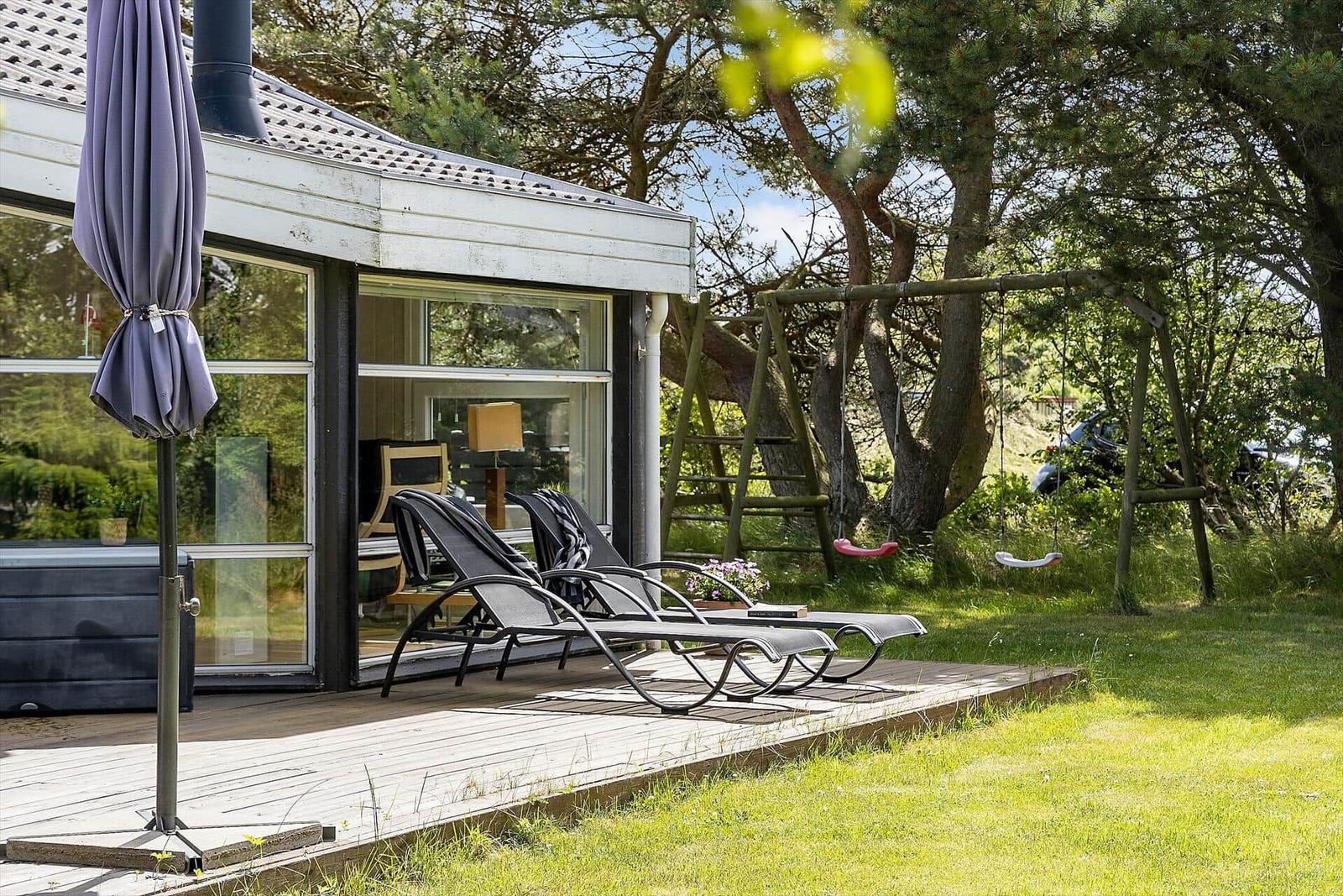 Terrasse mit Liegestühlen, Sonnenschirm und Schaukel im Grünen.