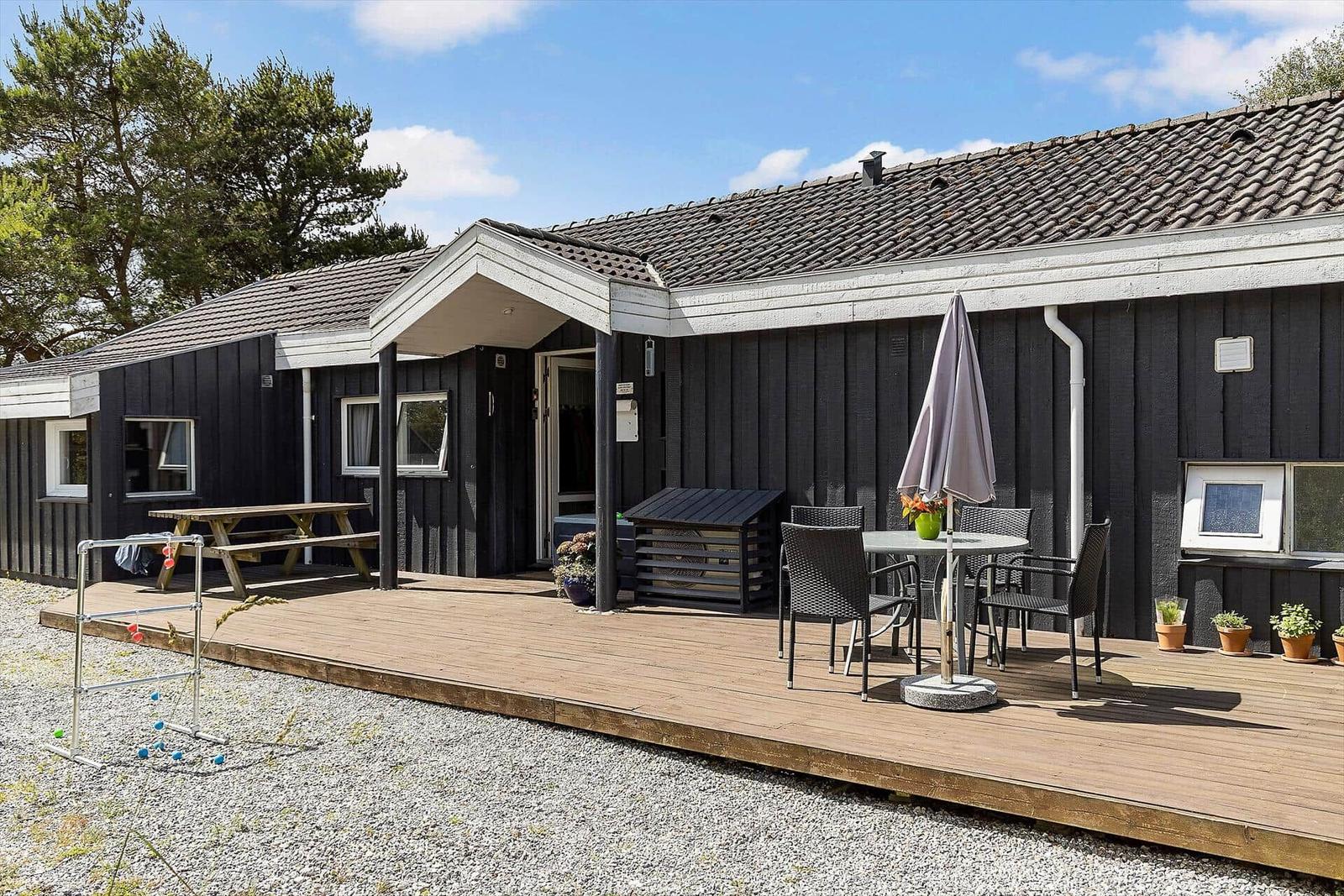 Schwarze Holzhütte mit Terrasse, Tisch, Stühlen und Sonnenschirm.