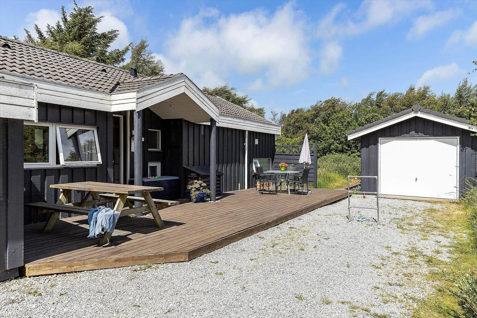Haus mit Holzterrasse, Picknicktisch, Gartenmöbel und Garage.