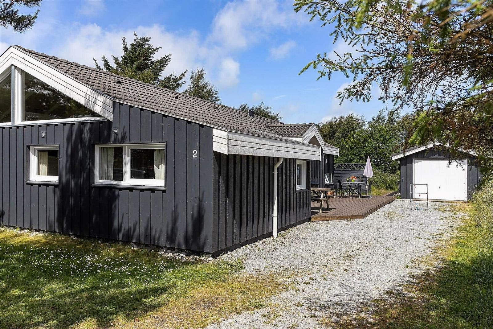 Schwarzes Holzhaus mit Terrasse und Garten. Nebenhaus mit weißer Tür.