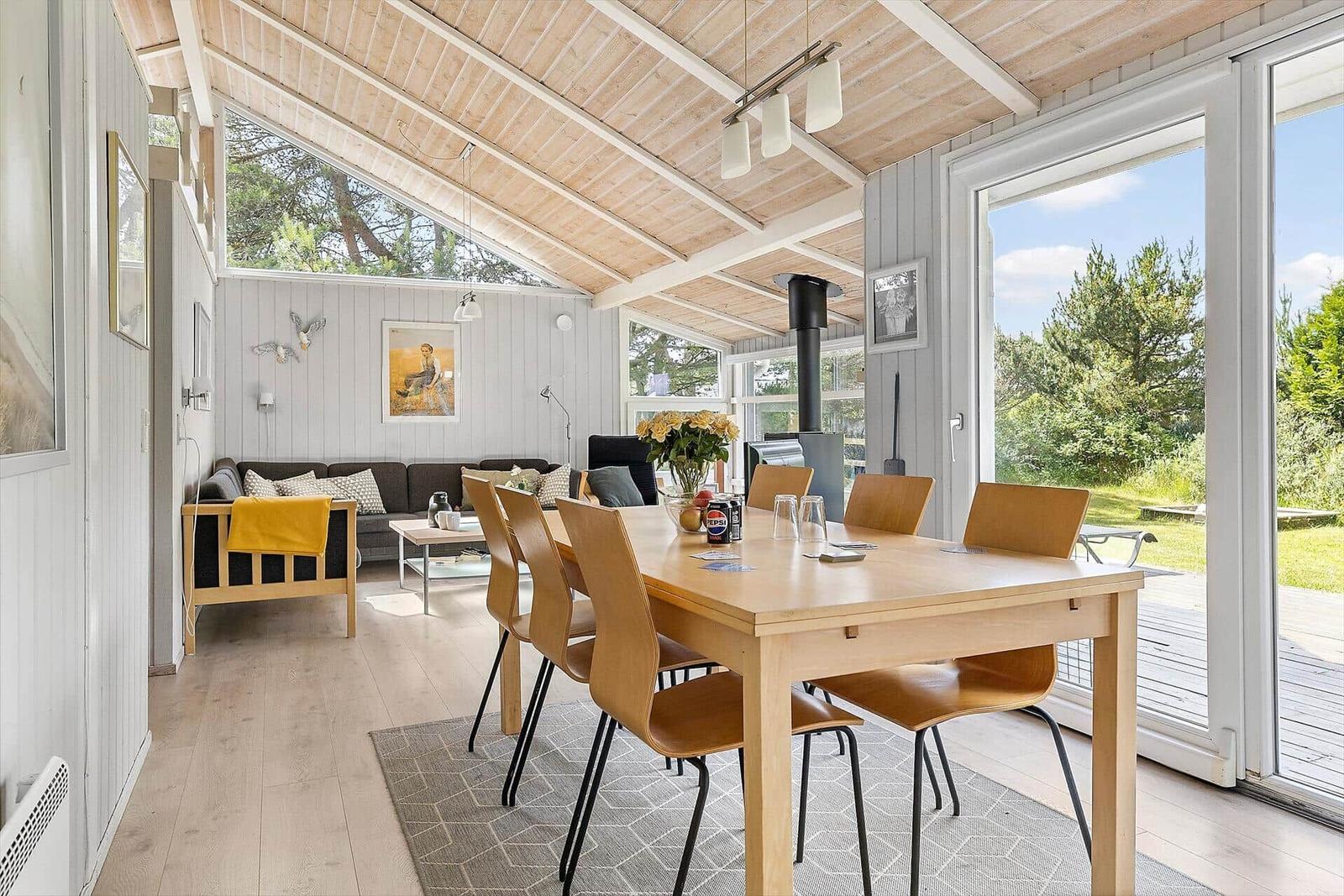 Esszimmer mit Tisch und Stühlen. Wohnbereich mit Sofa und Fenster. Holzdecke und Terrasse.