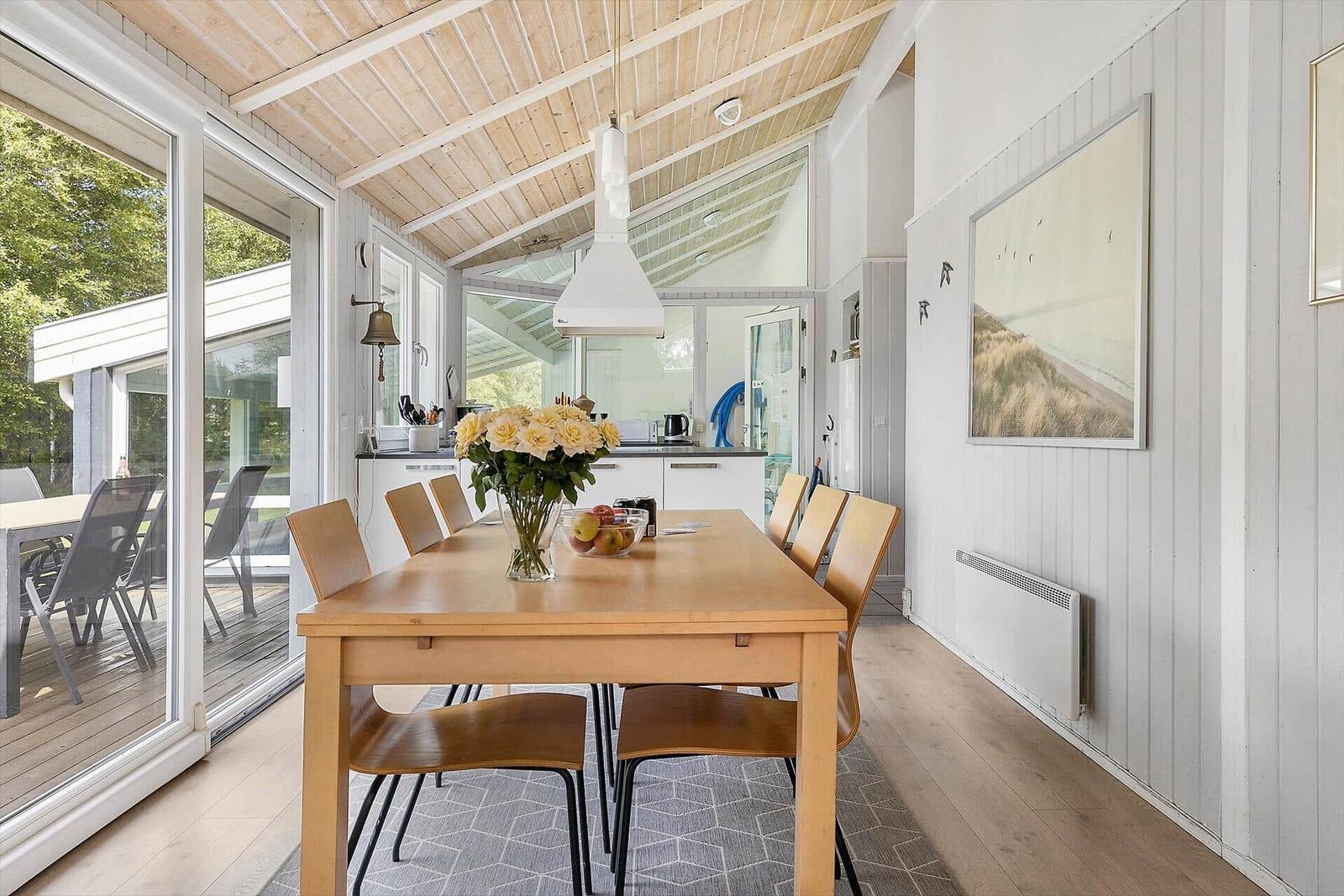 Essbereich mit Holztisch, Stühlen und Blumen. Küche und Terrasse sind sichtbar.
