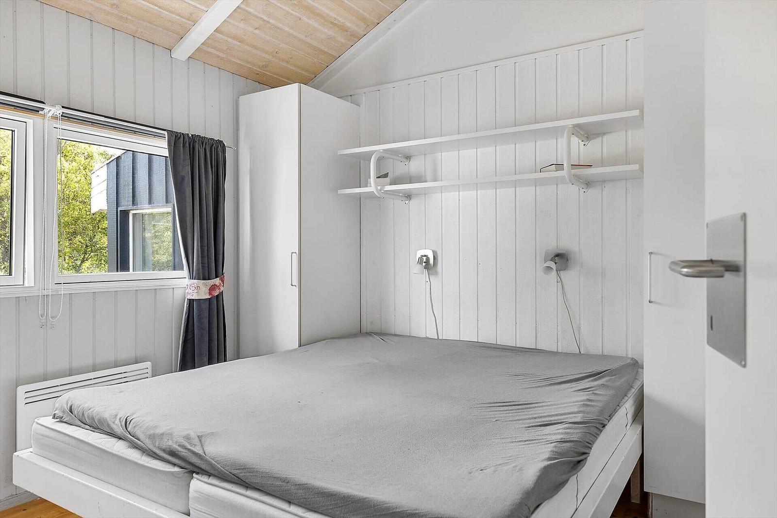 Schlafzimmer mit Bett, Schrank und Fenster. Wandregale und Steckdosen sind vorhanden.