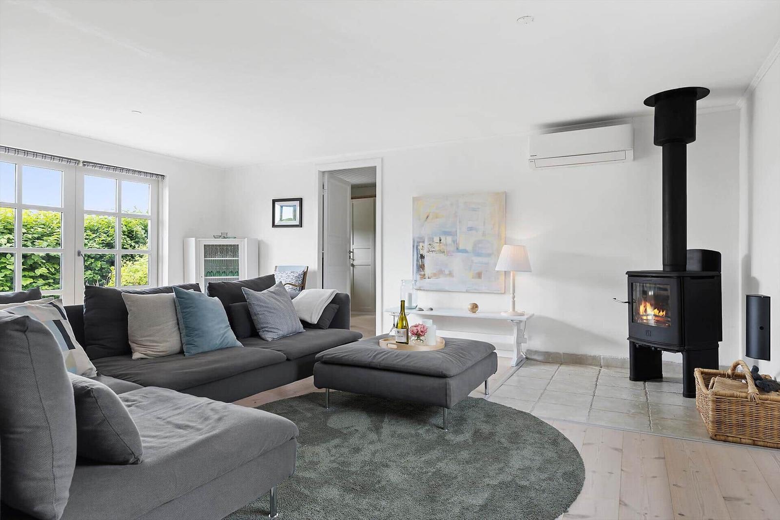 Wohnzimmer mit Sofa, Kamin und Fenster zur grünen Umgebung.