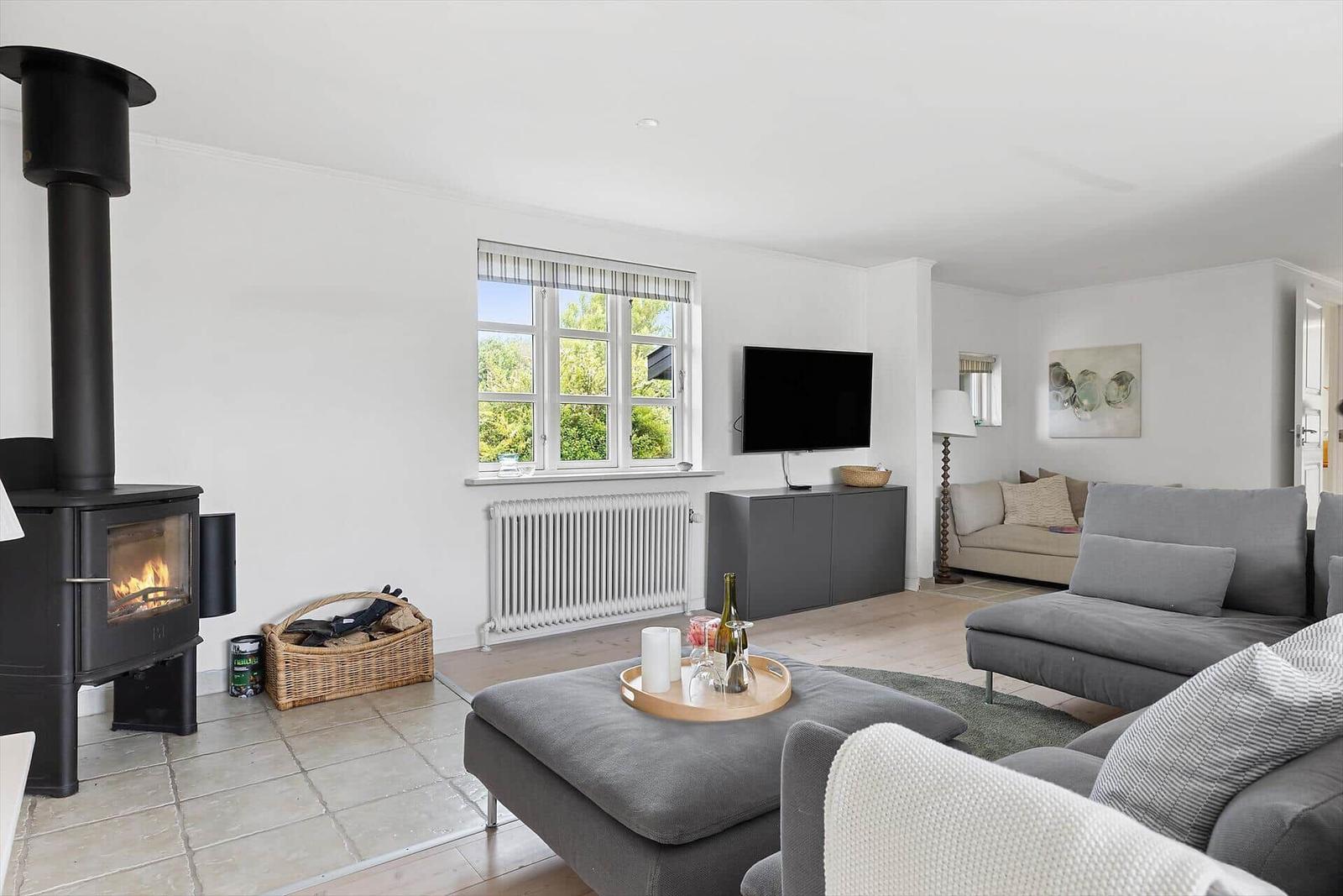 Wohnzimmer mit Kamin, Sofa und TV. Fenster mit Blick auf Grün.