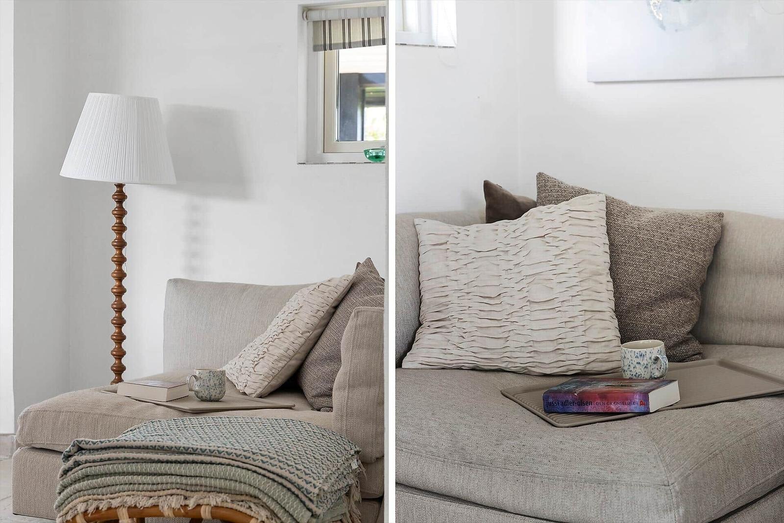 Ein Sofa mit Kissen und einer Decke. Eine Stehlampe und ein Fenster sind sichtbar.