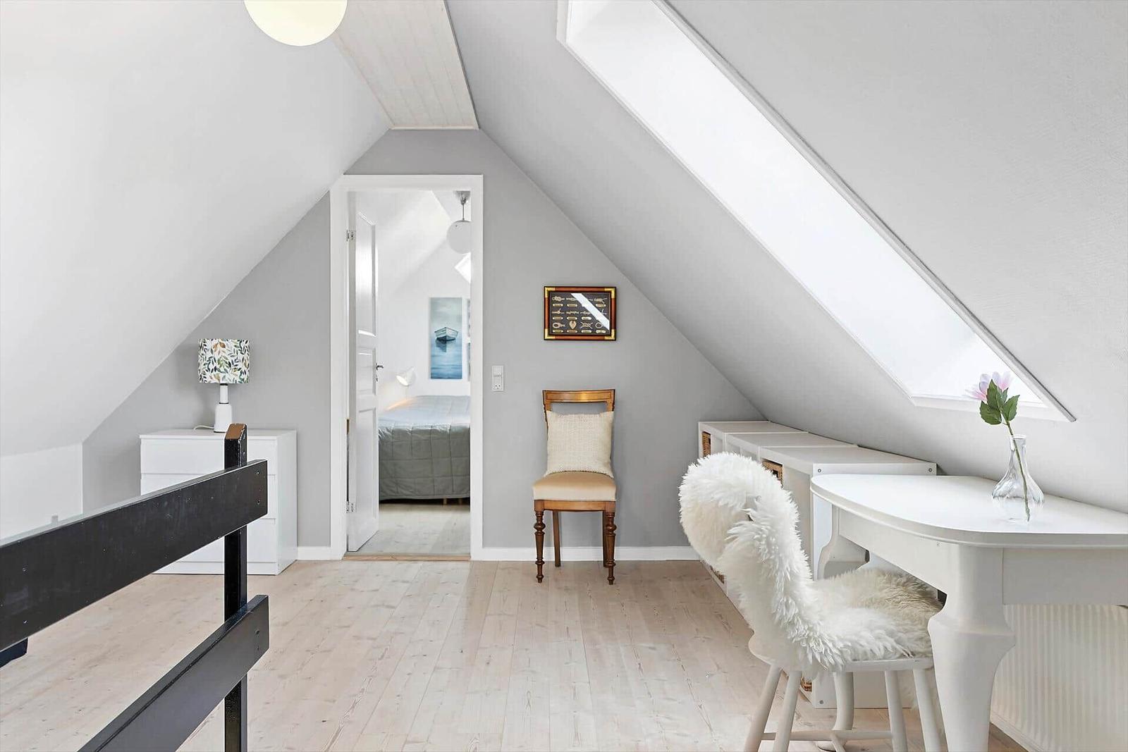 Dachgeschosszimmer mit Schreibtisch, Stuhl und Blick in Schlafzimmer