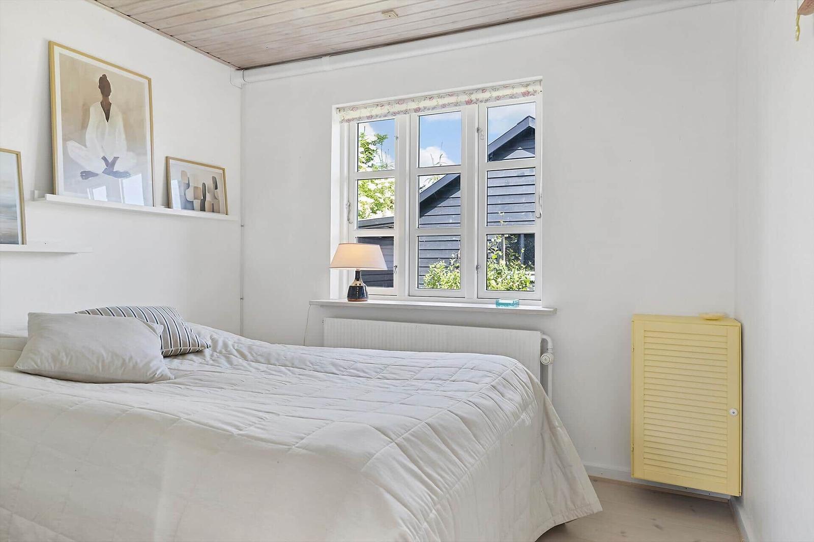 Schlafzimmer mit Bett, Fenster und gelbem Schrank.