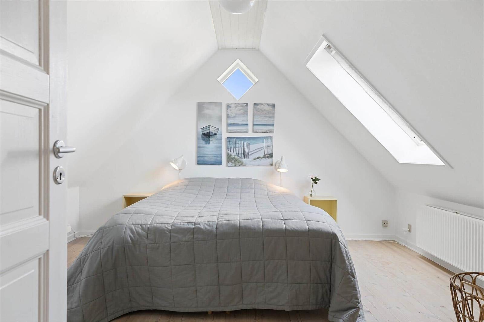 Schlafzimmer mit Dachschrägen, Dachfenster und Bett mit grauer Bettdecke.