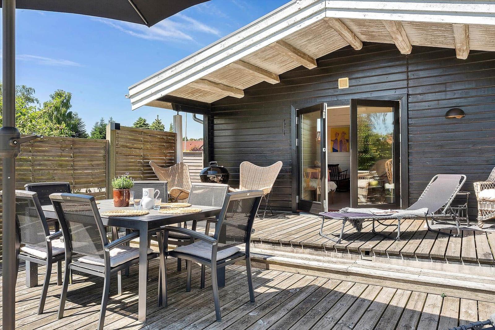 Deck with table, chairs, loungers, and grill. Wood wall and glass doors lead into the house.