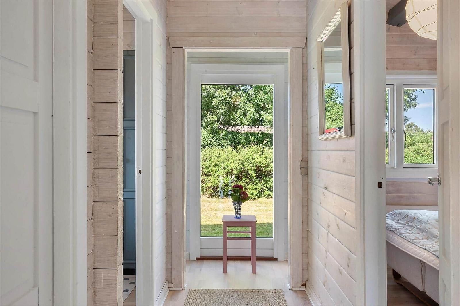 Hall with wooden walls, door to garden, mirror, and bed in background.