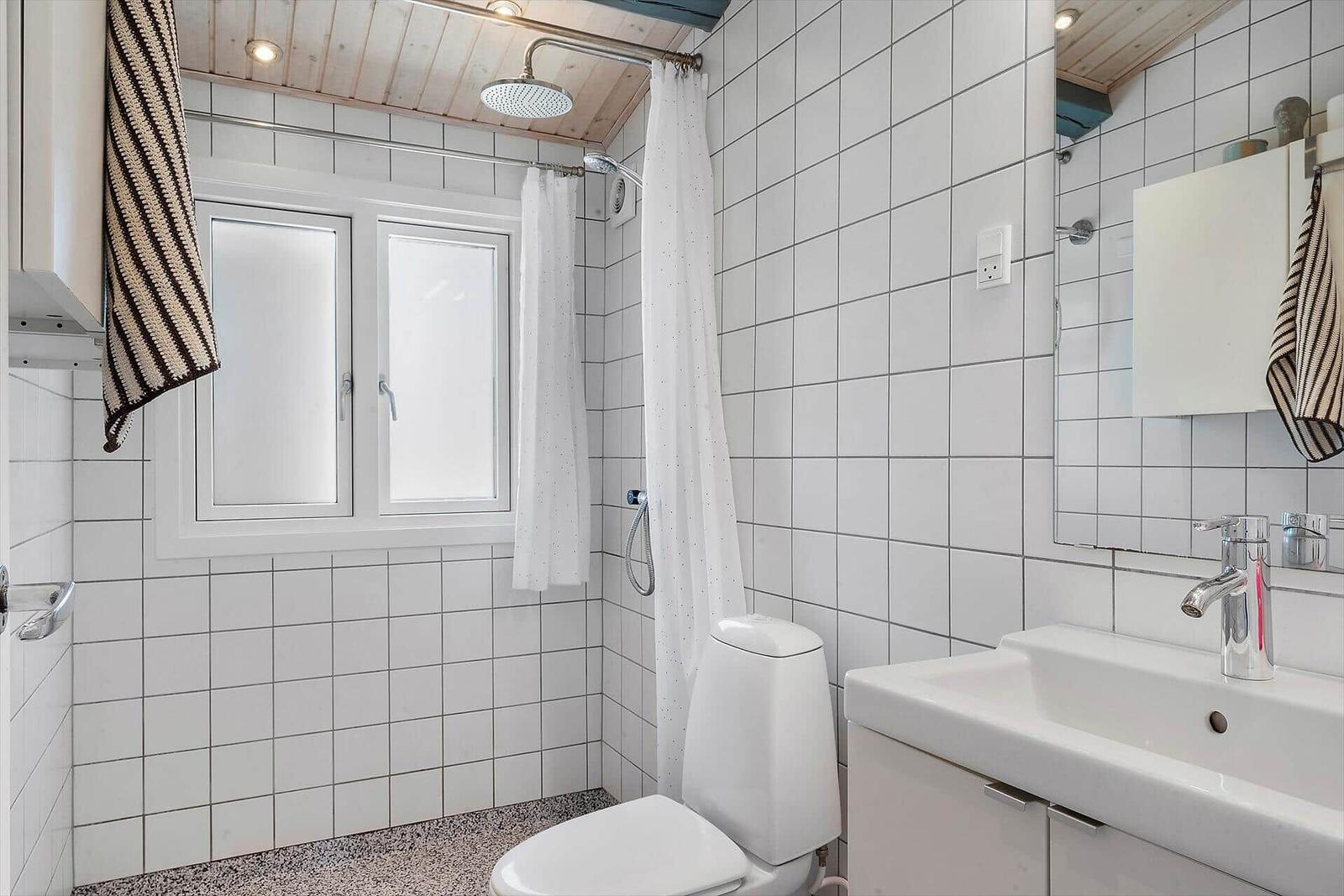 Bathroom with shower, toilet, and sink. White tiles and wooden ceiling.