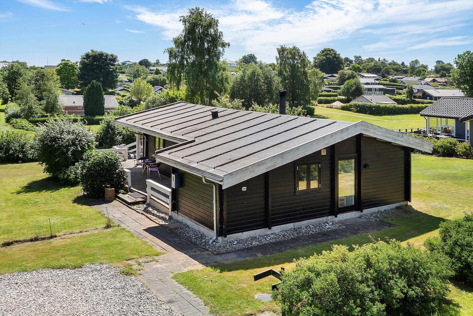 Wooden house with terrace and garden. Surrounded by green areas and trees.