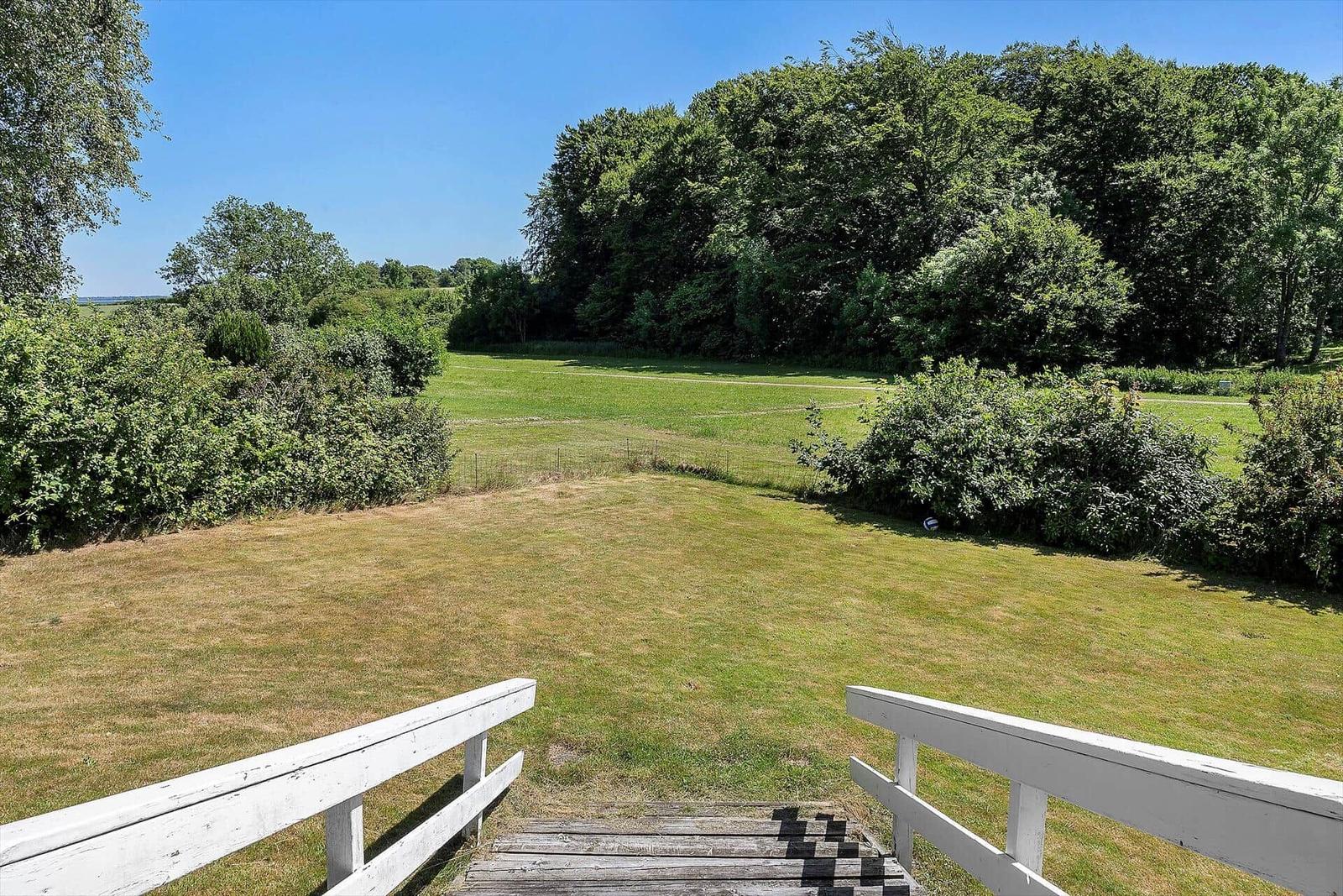 Large garden with view of forest and meadow. Wooden steps with white railing.