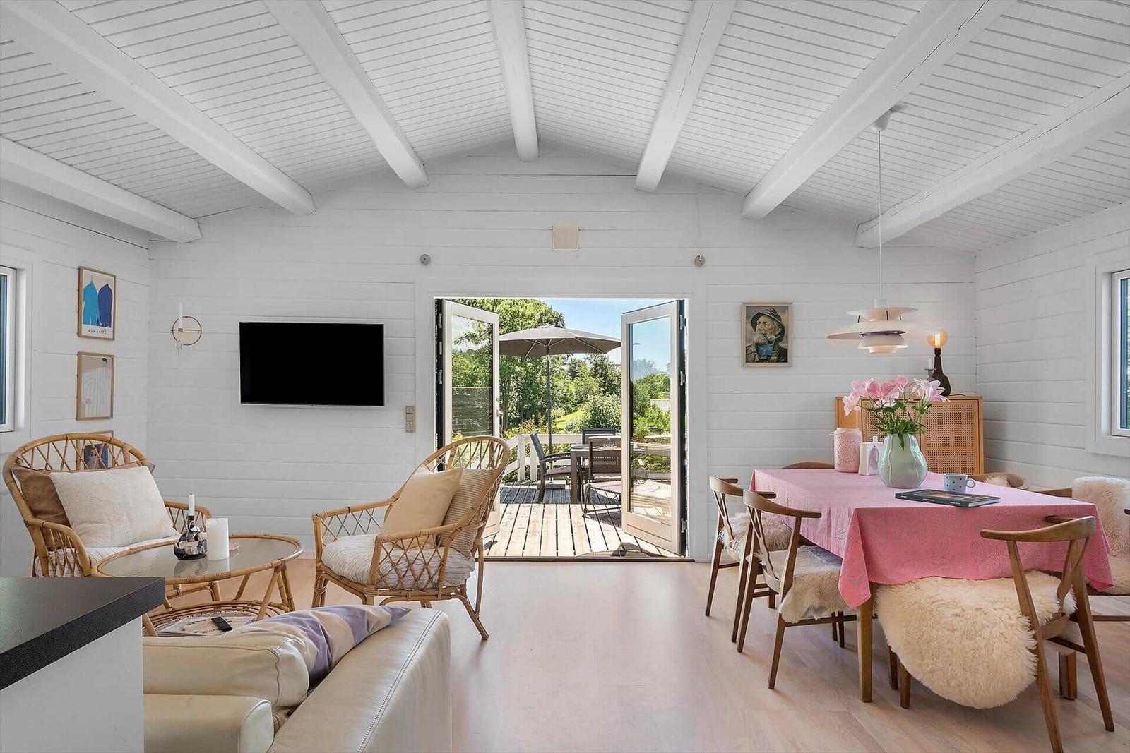 Living and dining area with table, chairs, and TV. Entrance to terrace with garden.