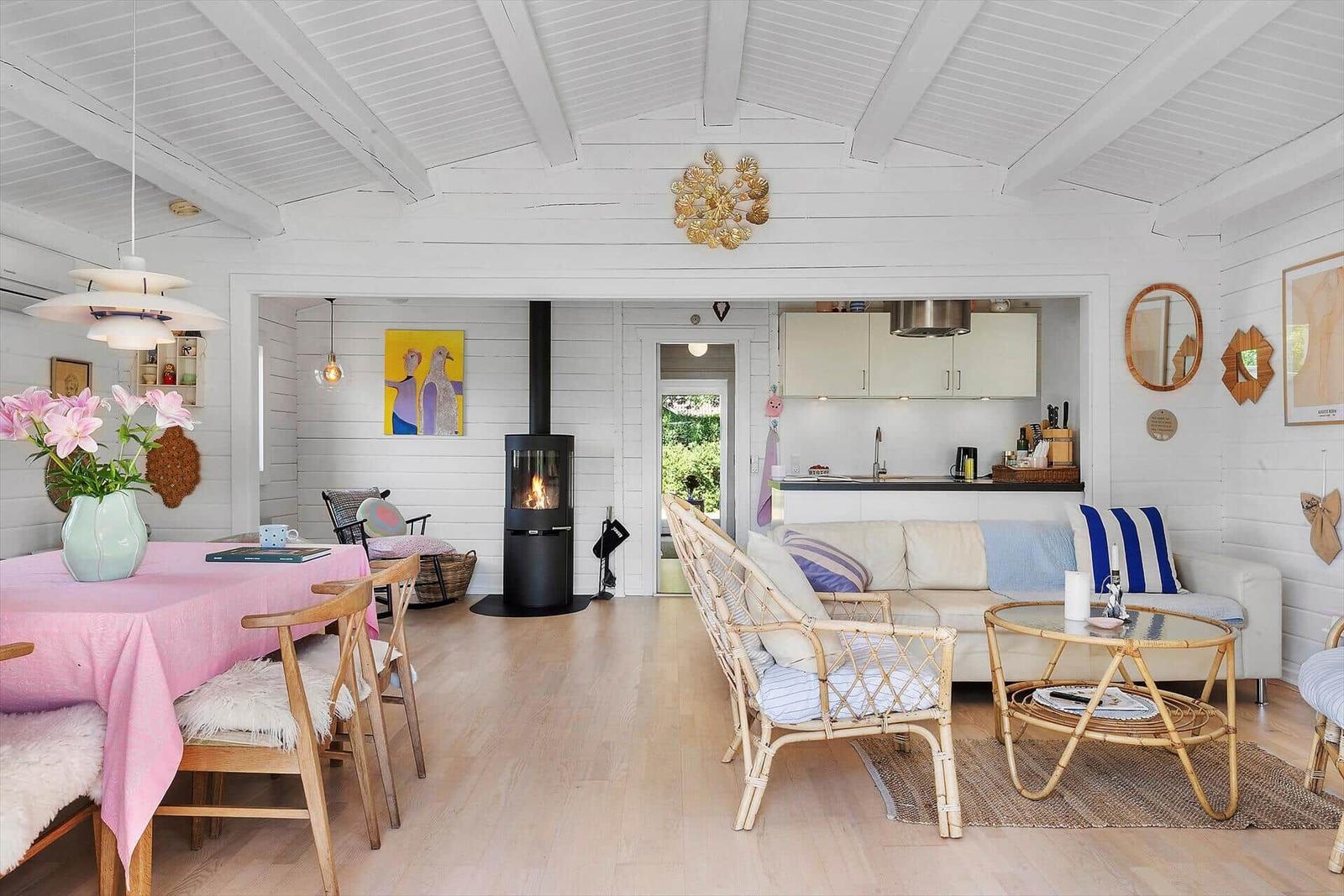Living room with dining table, sofa, and wood-burning stove. White walls and wooden floor.