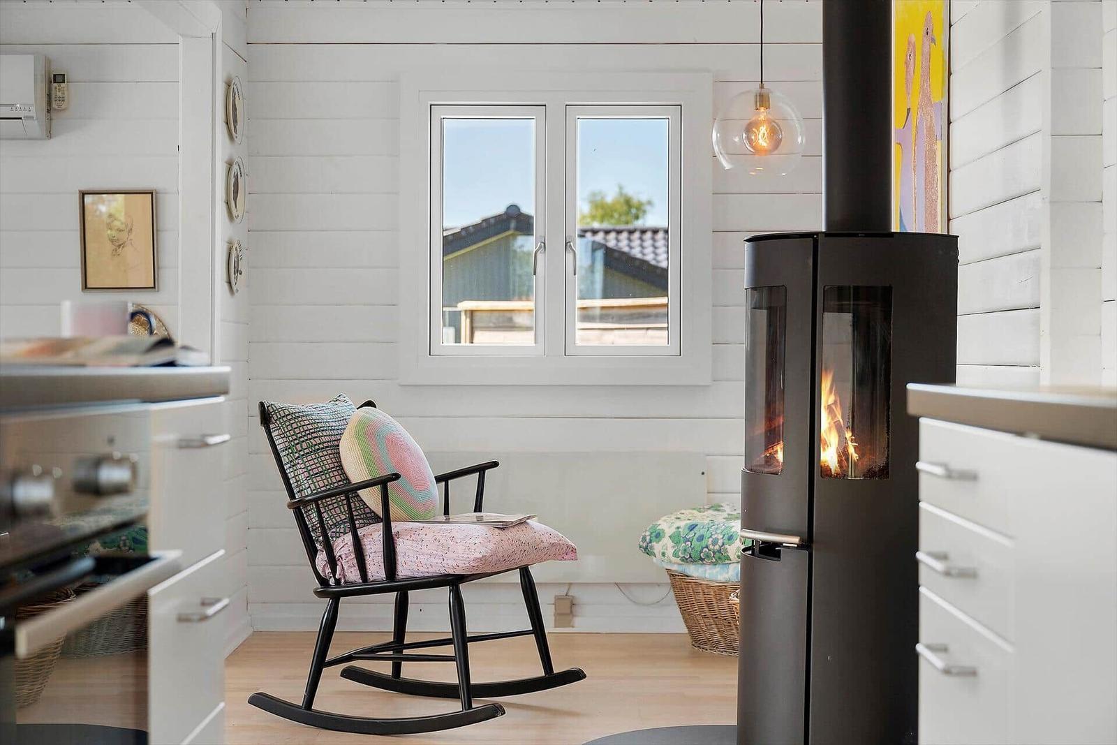 A room with a rocking chair, wood stove, and window overlooking outside.