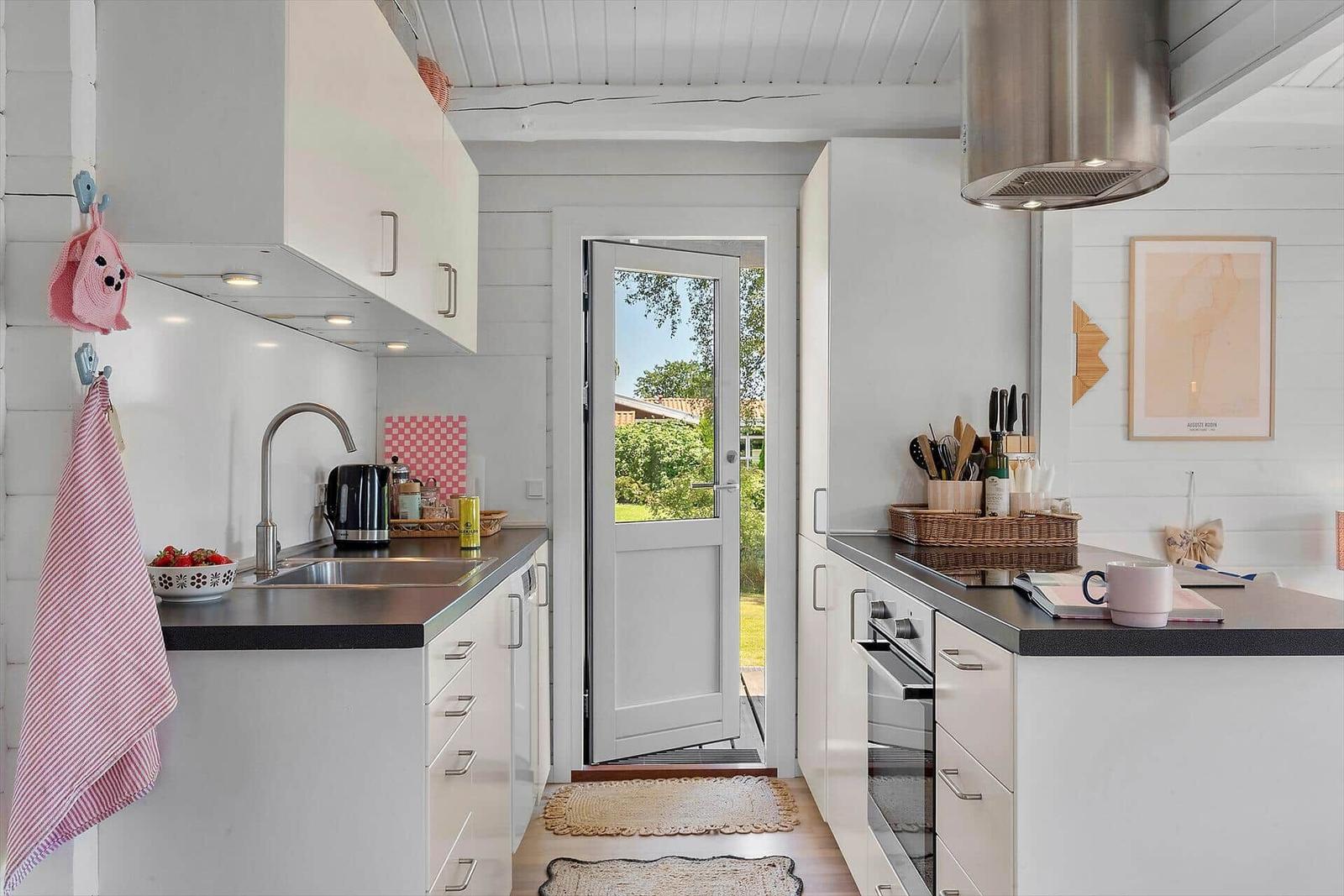 Kitchen with white cabinets, stainless steel sink, and door to the garden.