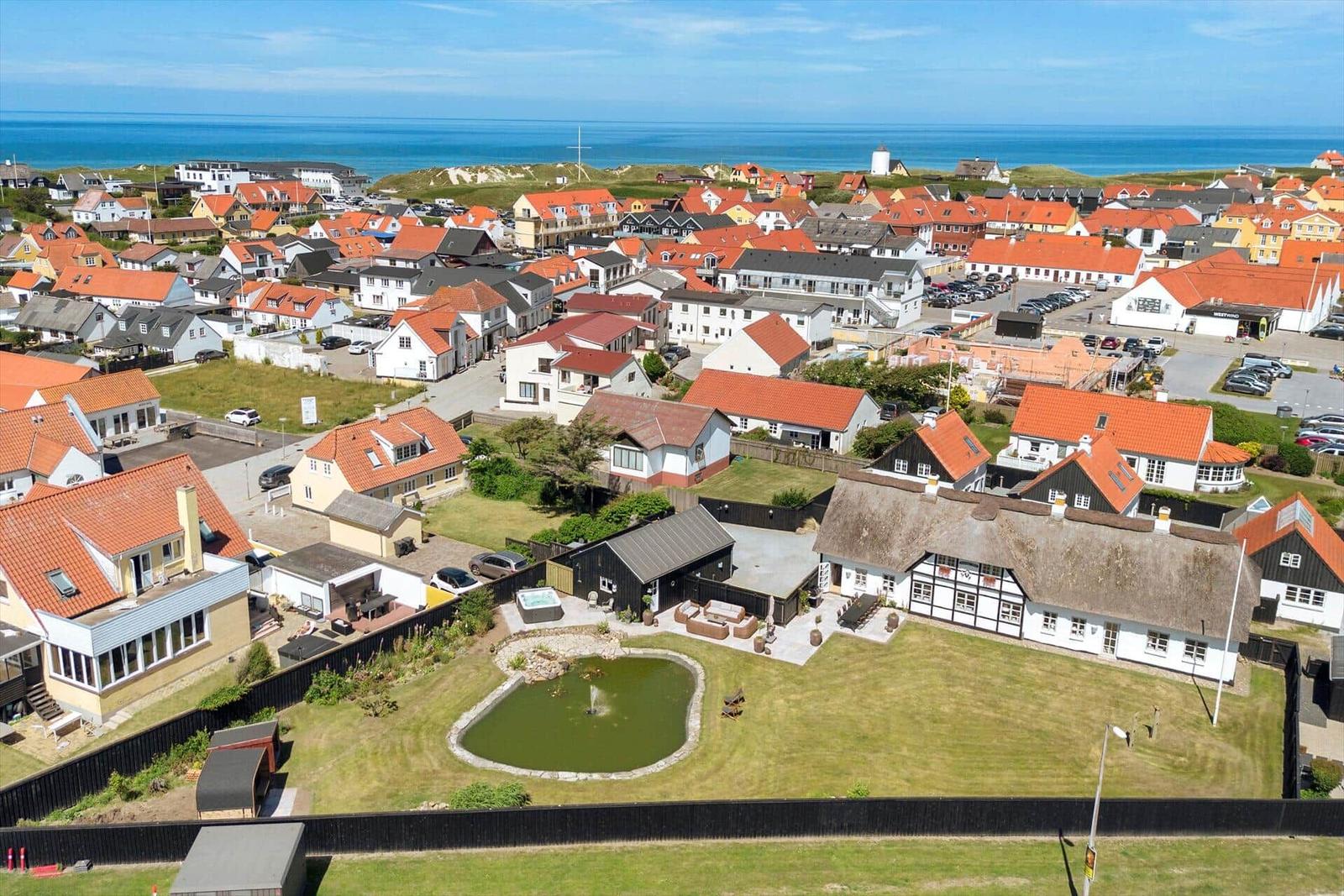 House with garden, pond, and view of coastal town with red roofs.