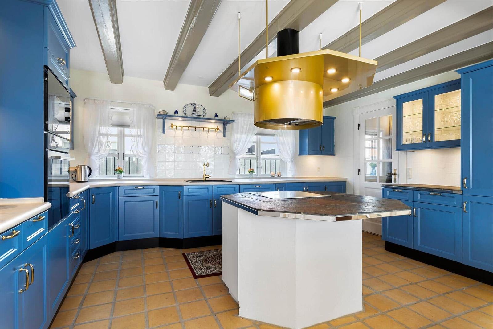 Kitchen with blue cabinets, white island, and gold range hood.