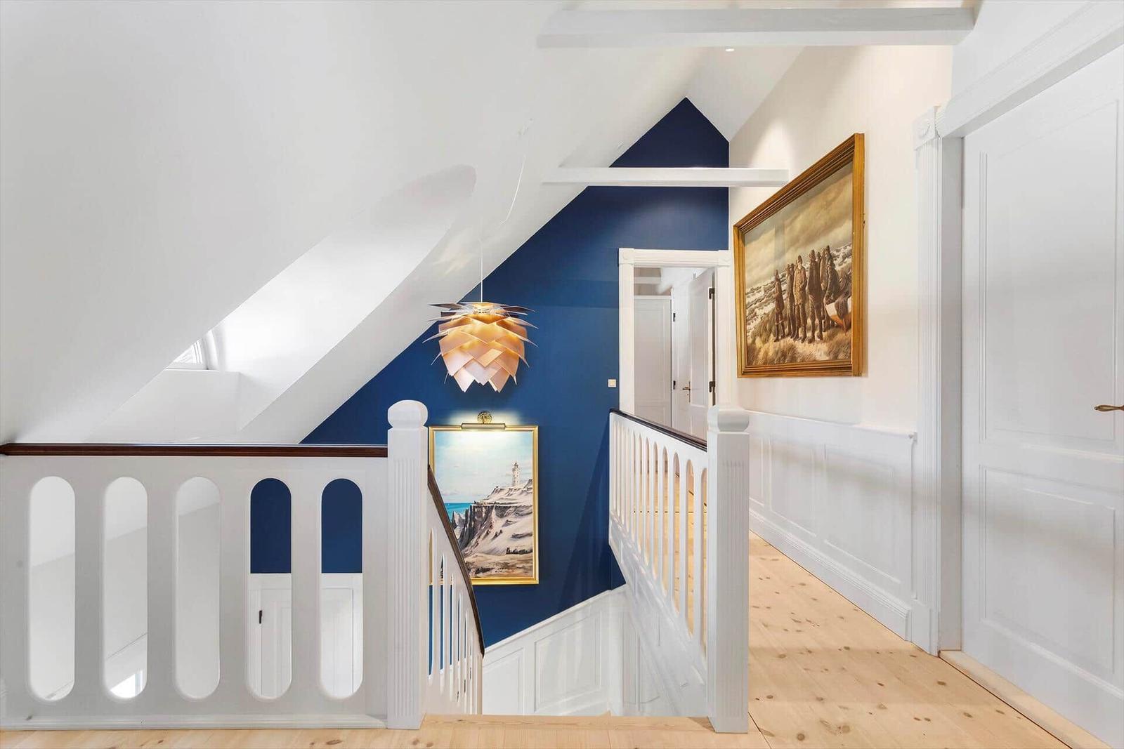 Hallway with blue wall, wooden floor, and artwork on the walls.
