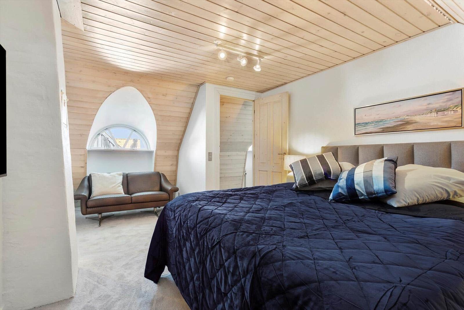 Bedroom with bed, sofa, and wooden ceiling.