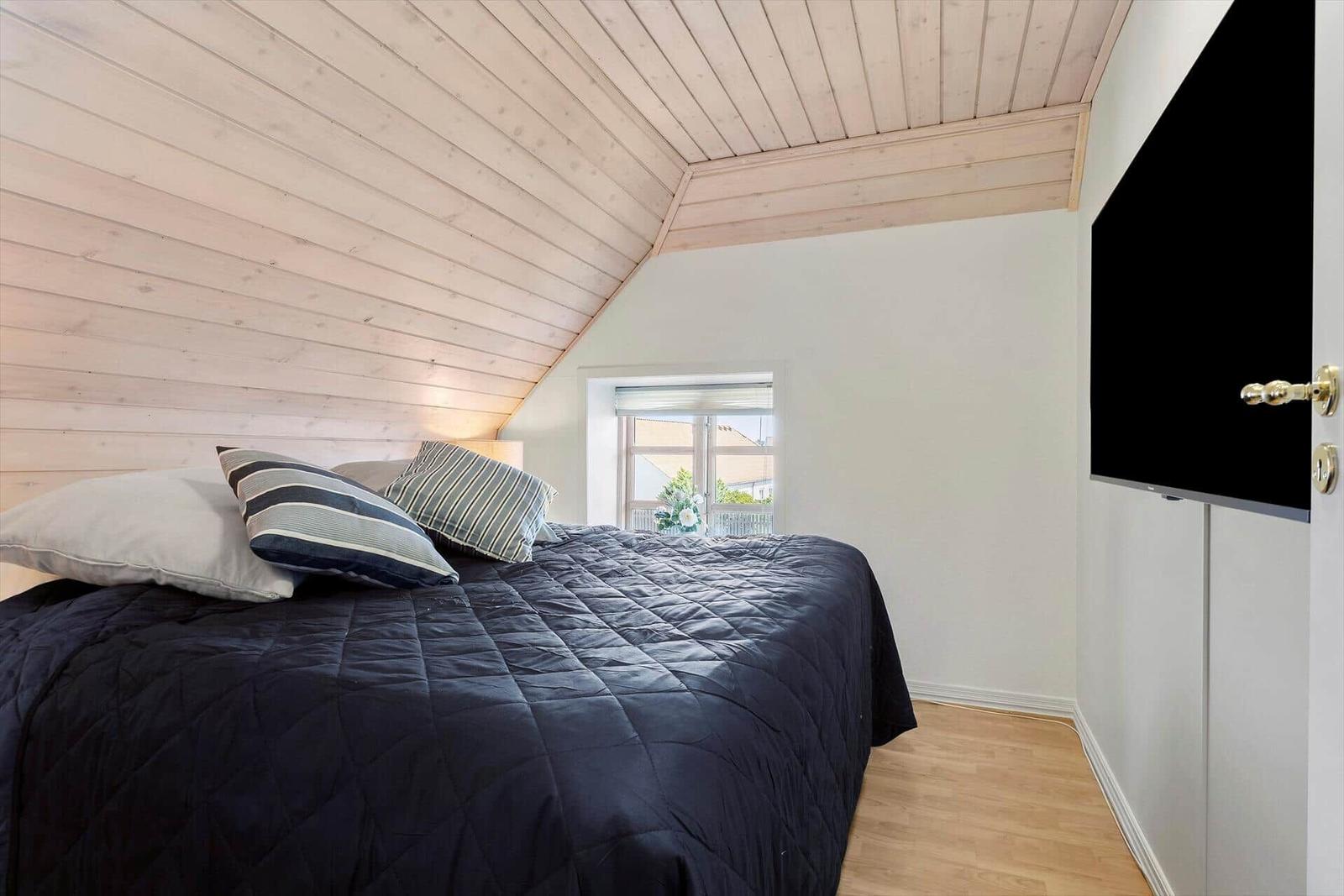 Bedroom with sloped ceiling, bed, and TV mounted on wall.