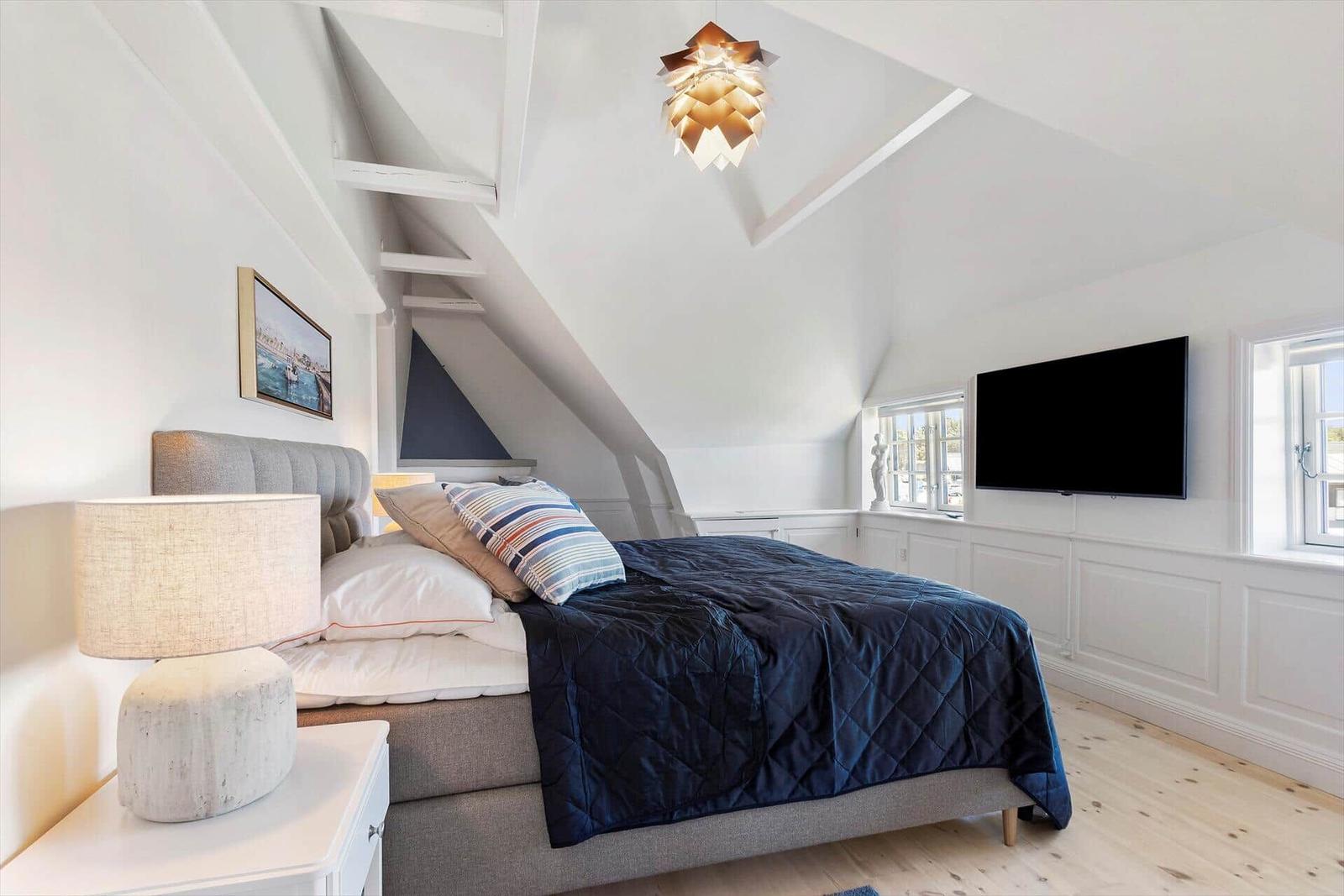 Bedroom with sloped ceiling, bed, TV, and windows.