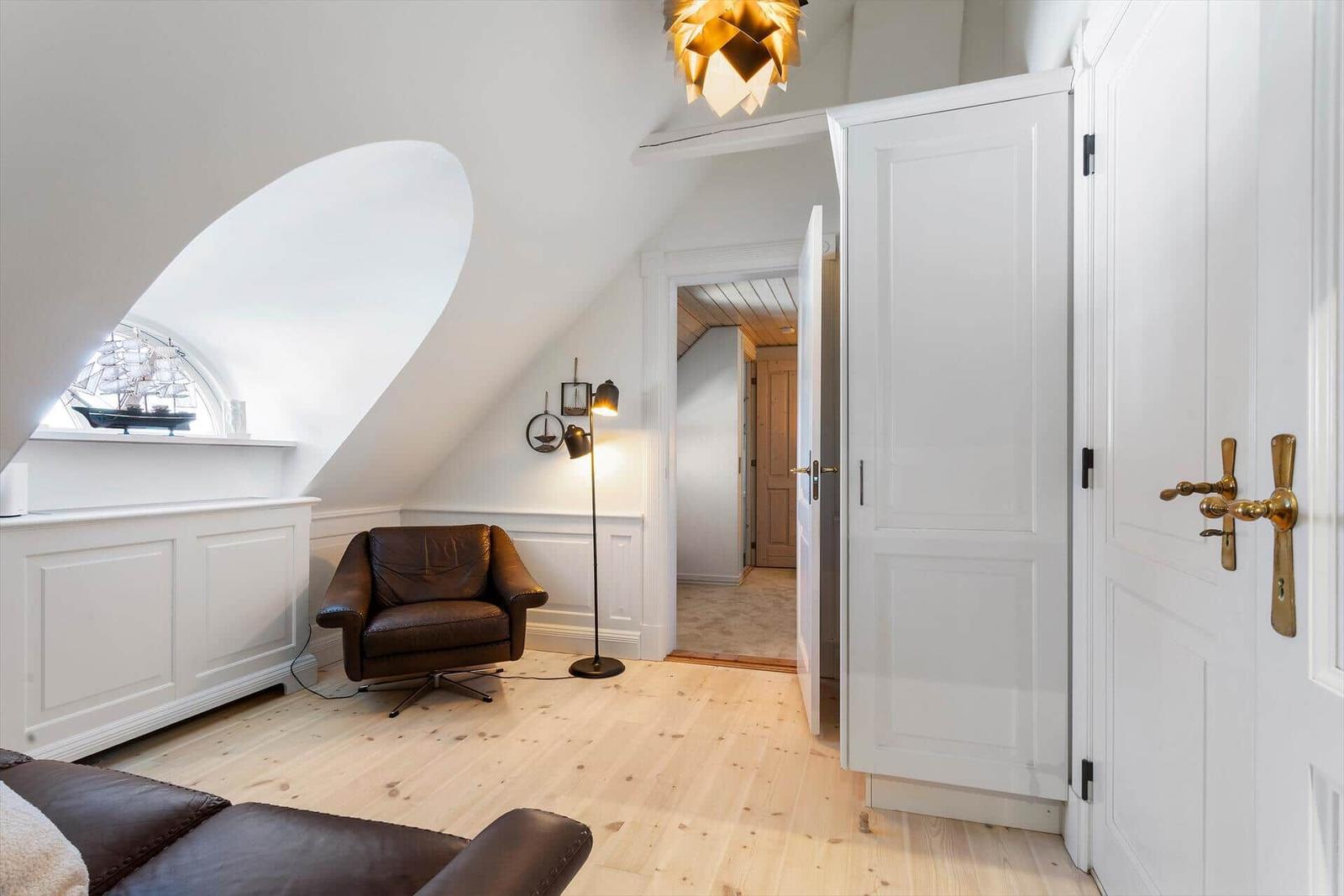 Room with brown leather chair, wooden floor, and sloped ceiling with window.