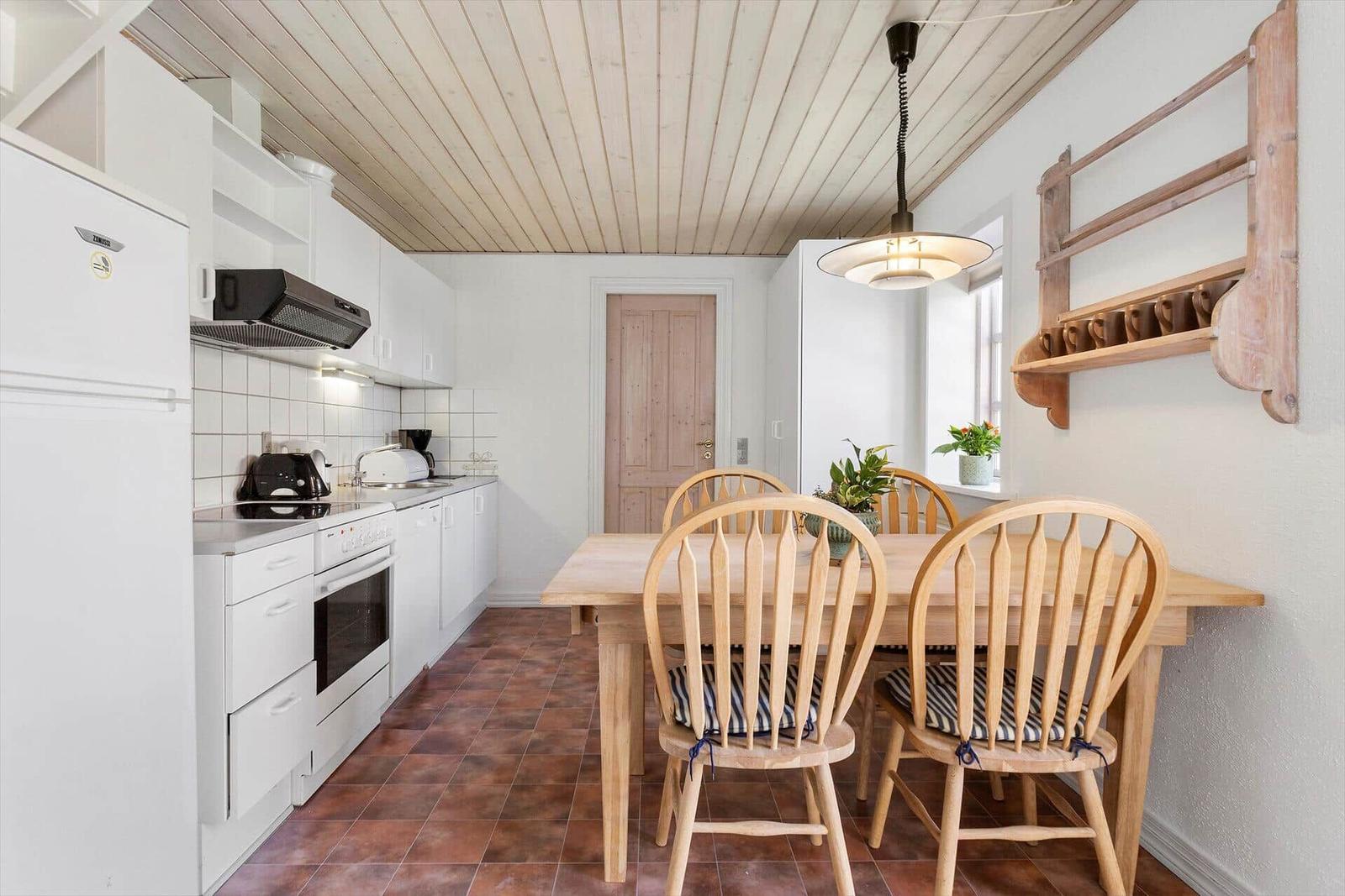 Kitchen with dining table and wooden chairs, white cabinets and wooden ceiling.