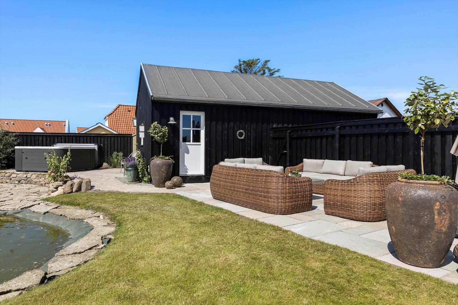 Black garden house with terrace, seating area, and pond.