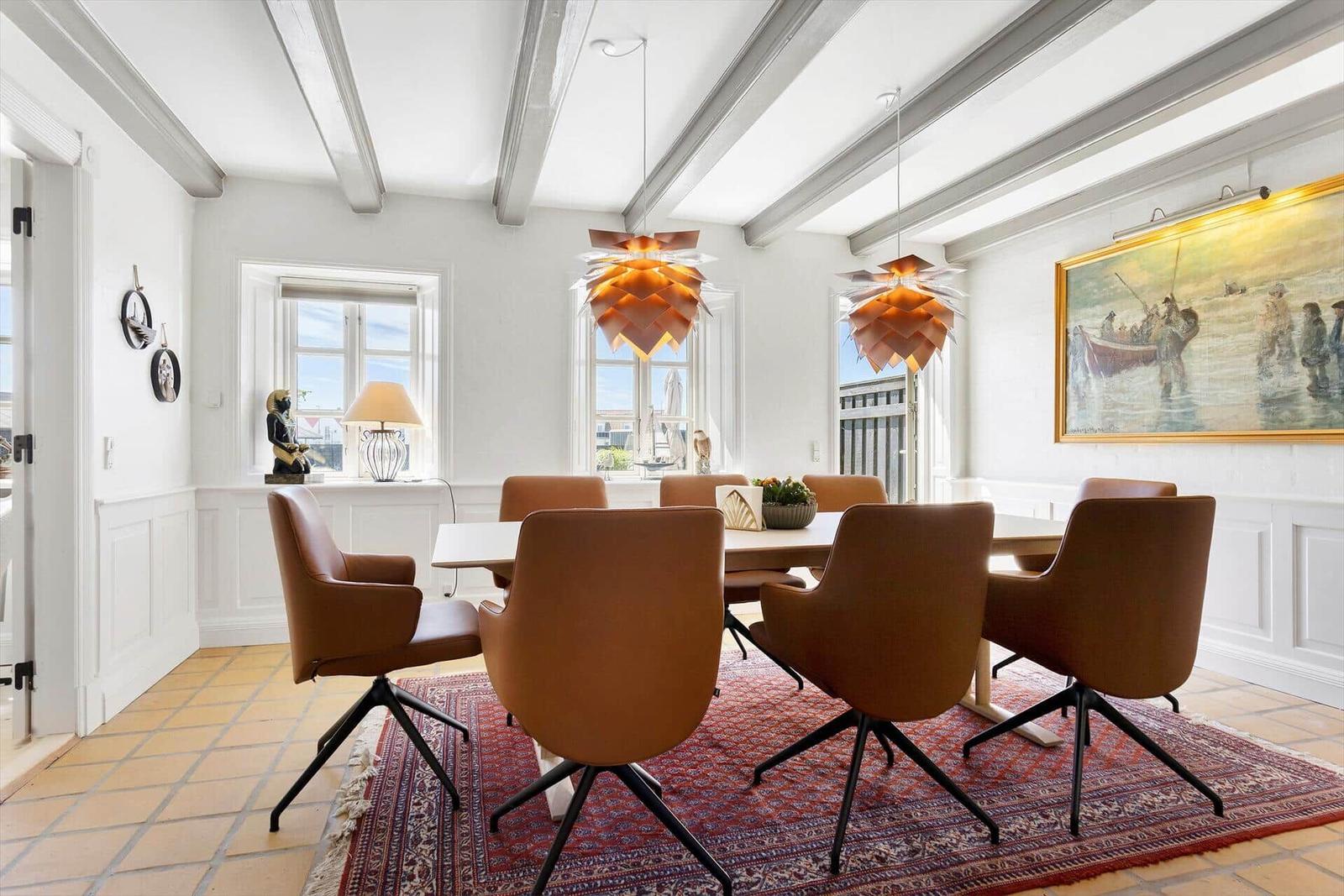 Dining room with table, chairs, ceiling beams, and wall painting.