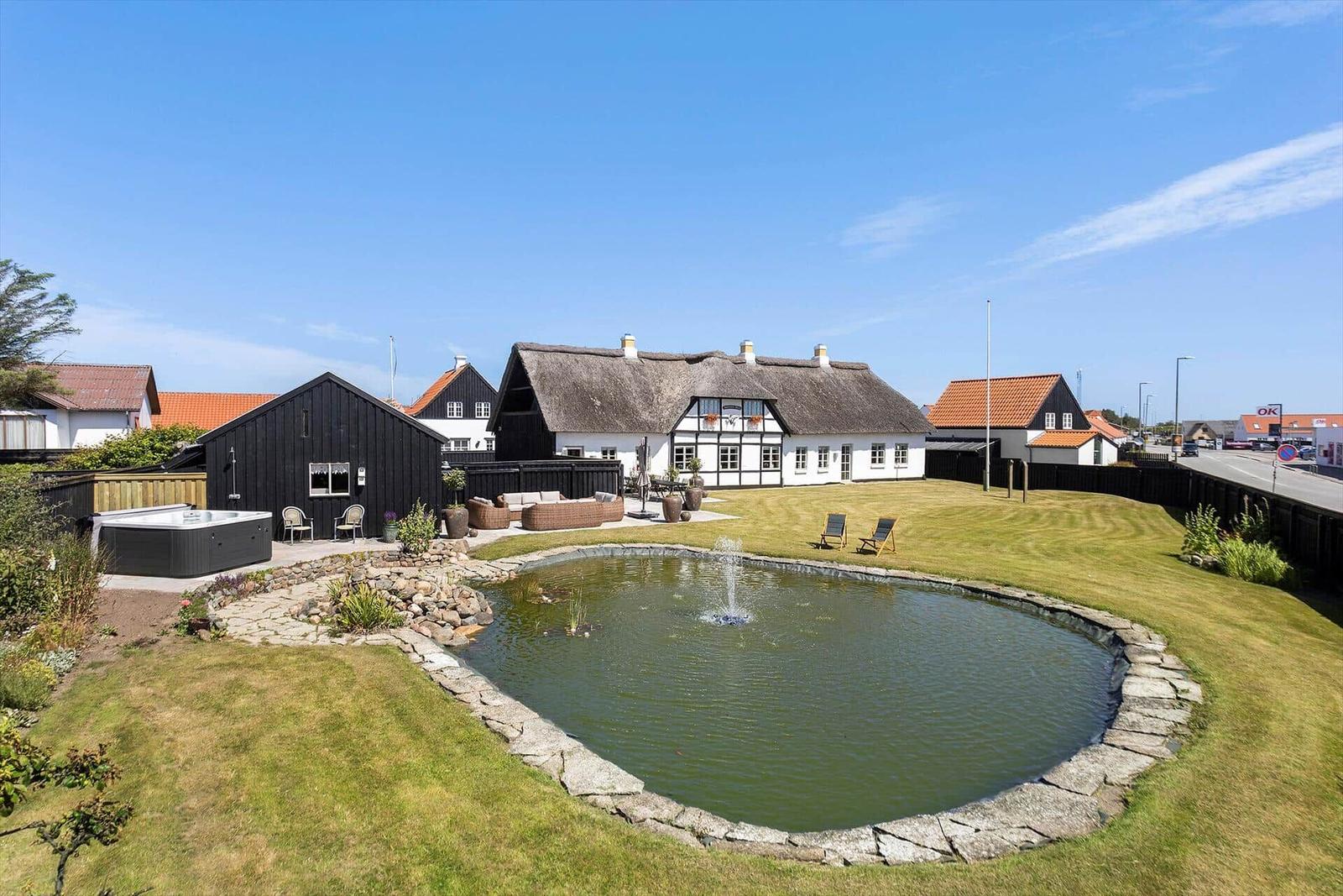 House with pond, hot tub, and garden area. Traditional architecture with thatched roof.
