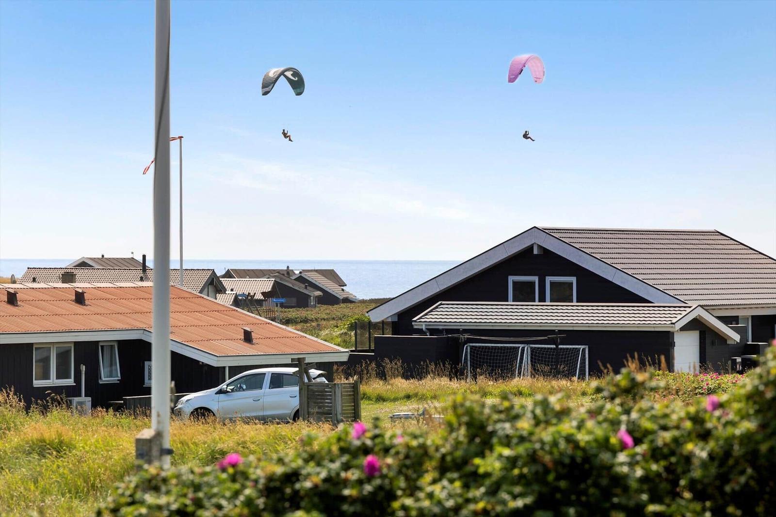 Zwei Paraglider fliegen über Häuser mit Blick auf das Meer.