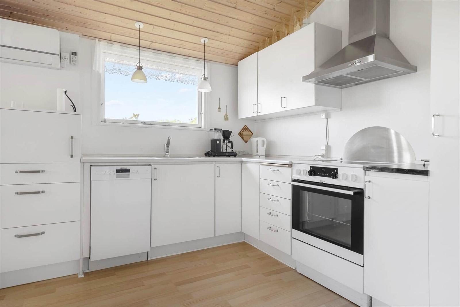 Küche mit weißen Schränken, Herd und Spüle. Holzdecke und Fenster mit Vorhang.