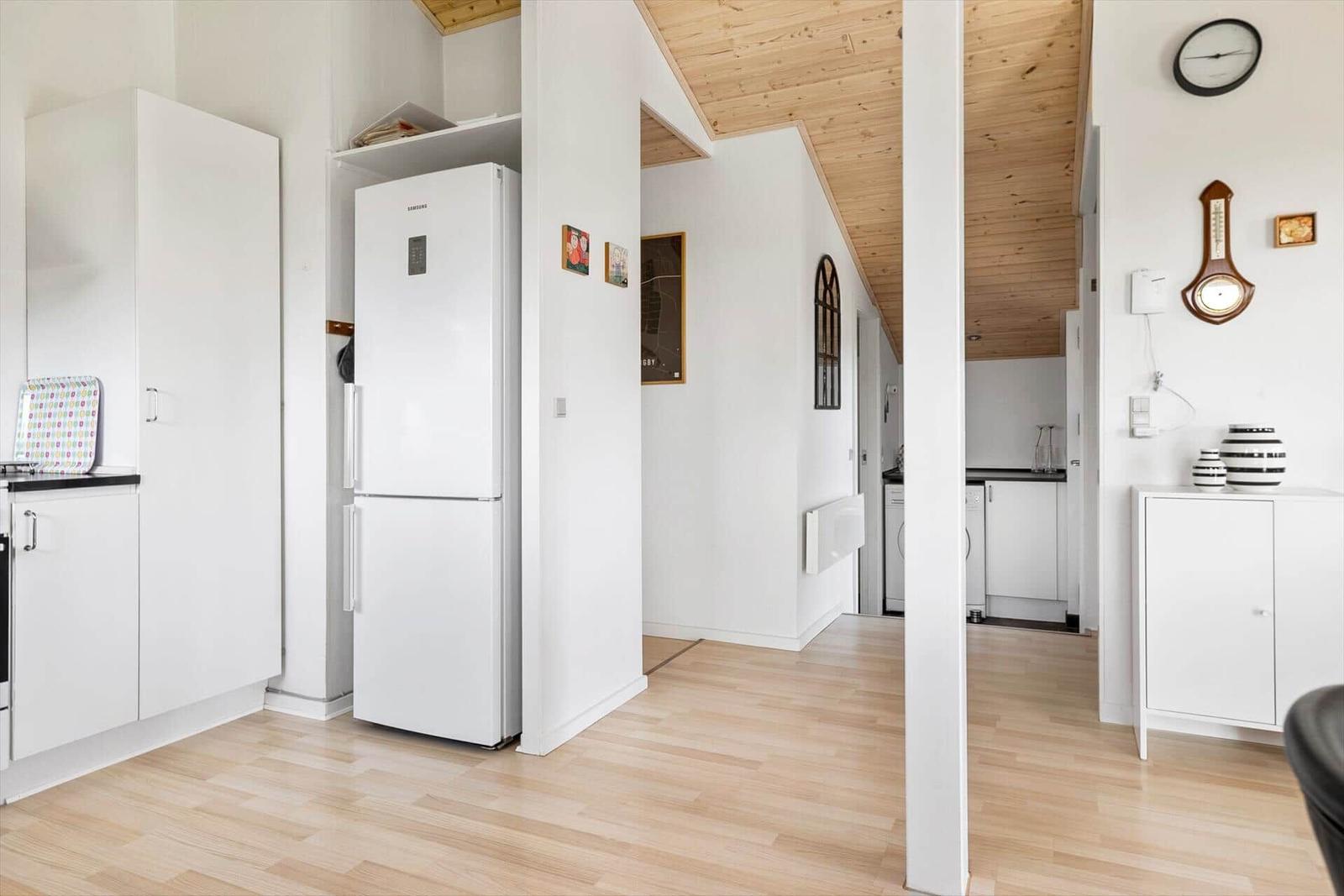 Küche mit Kühlschrank und weißen Schränken. Holzdecke und -boden.