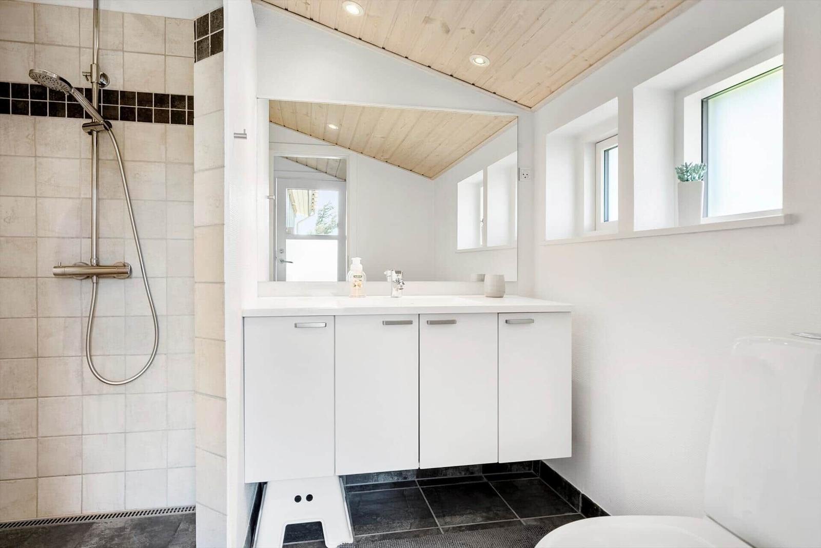 Badezimmer mit Dusche, Waschbecken und Toilette. Holzdecke und Fenster.