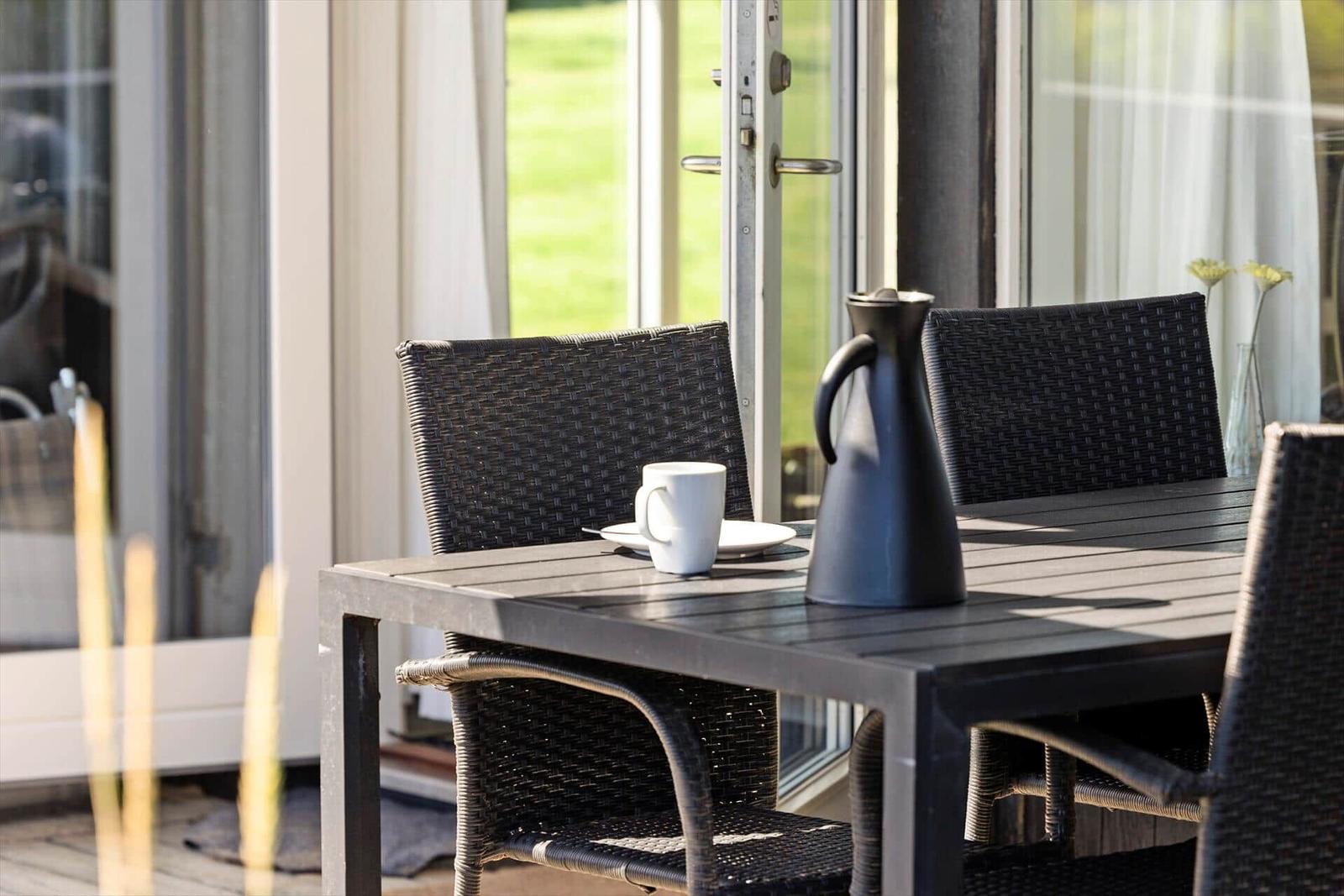 Terrassentisch mit Stühlen, Kaffeetasse und Kanne vor Glasfront.