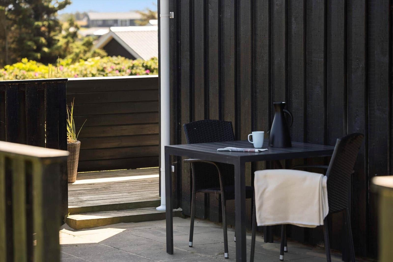 Terrasse mit Tisch, zwei Stühlen, Kaffeetasse und Kanne. Blick auf grüne Vegetation.