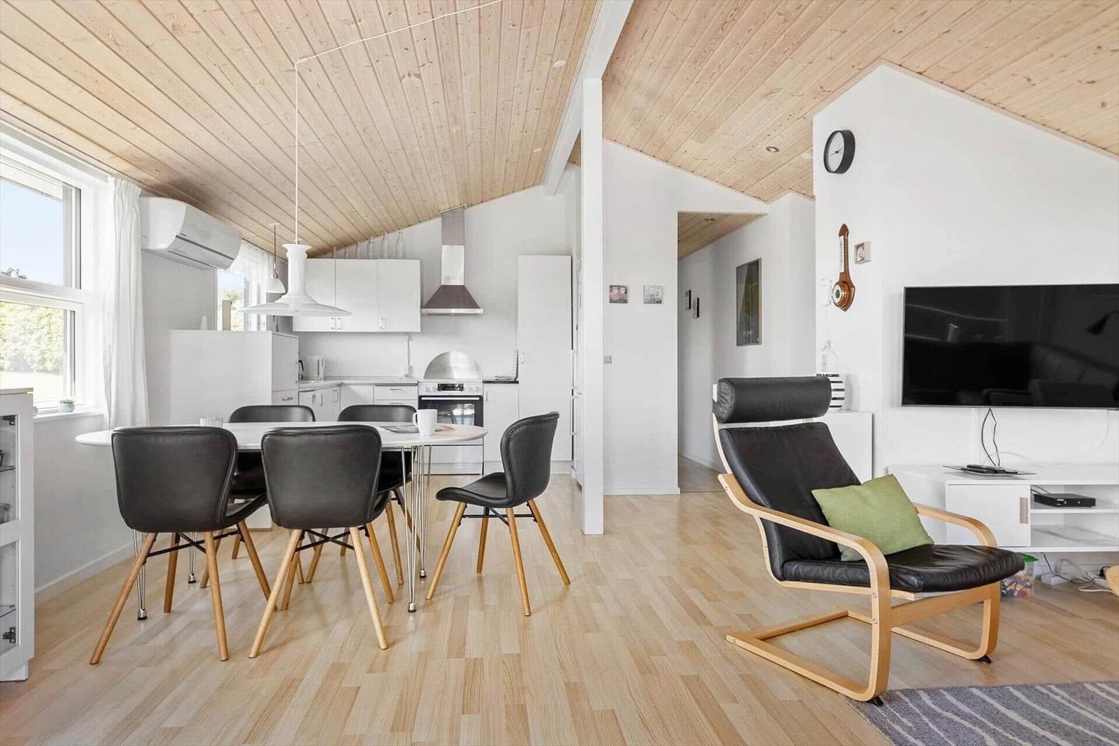 Wohnküche mit Essbereich und Sessel. Holzdecke und -boden.